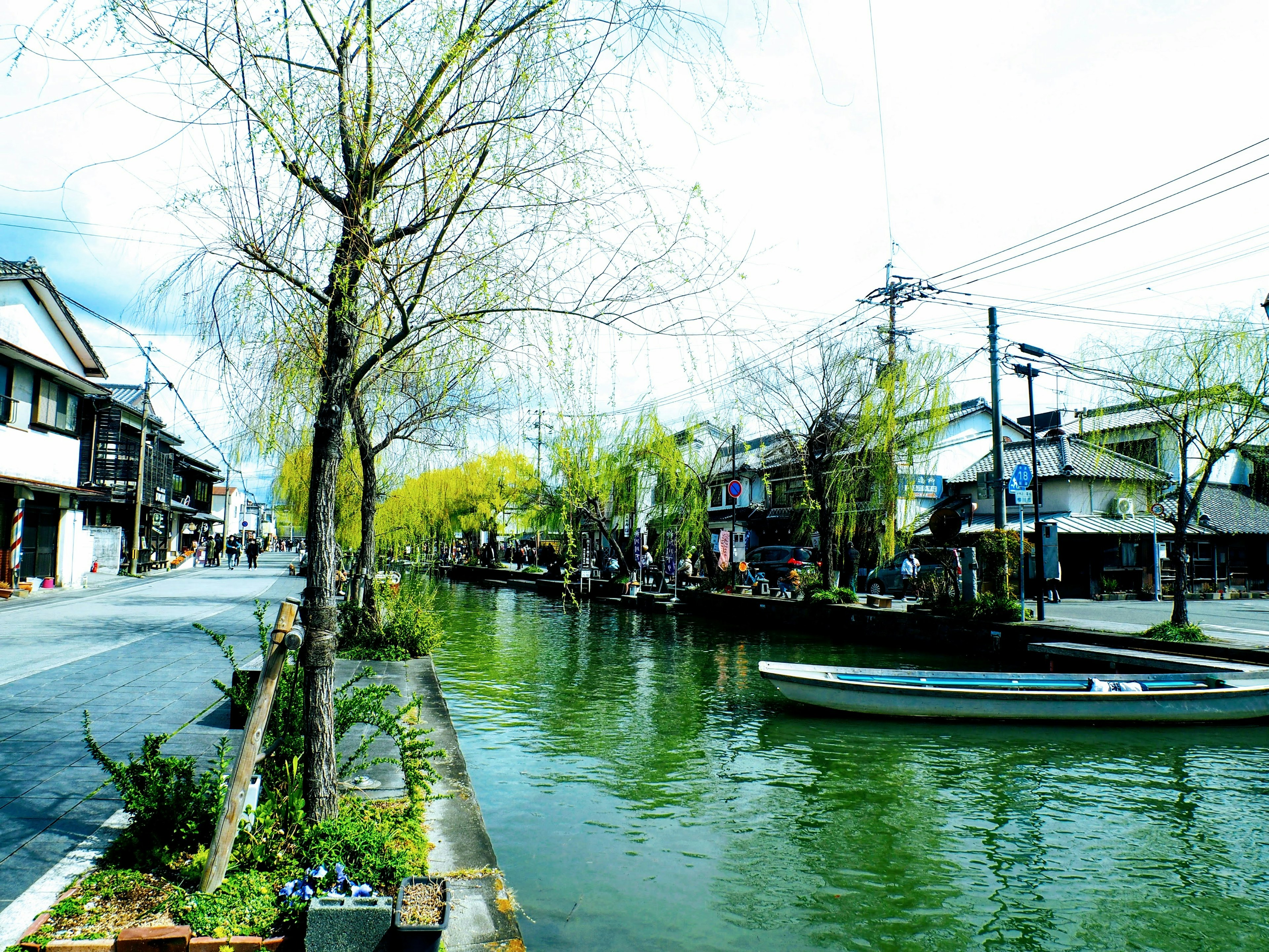 Pemandangan tenang di tepi sungai dengan pohon willow dan bangunan tradisional di dekatnya