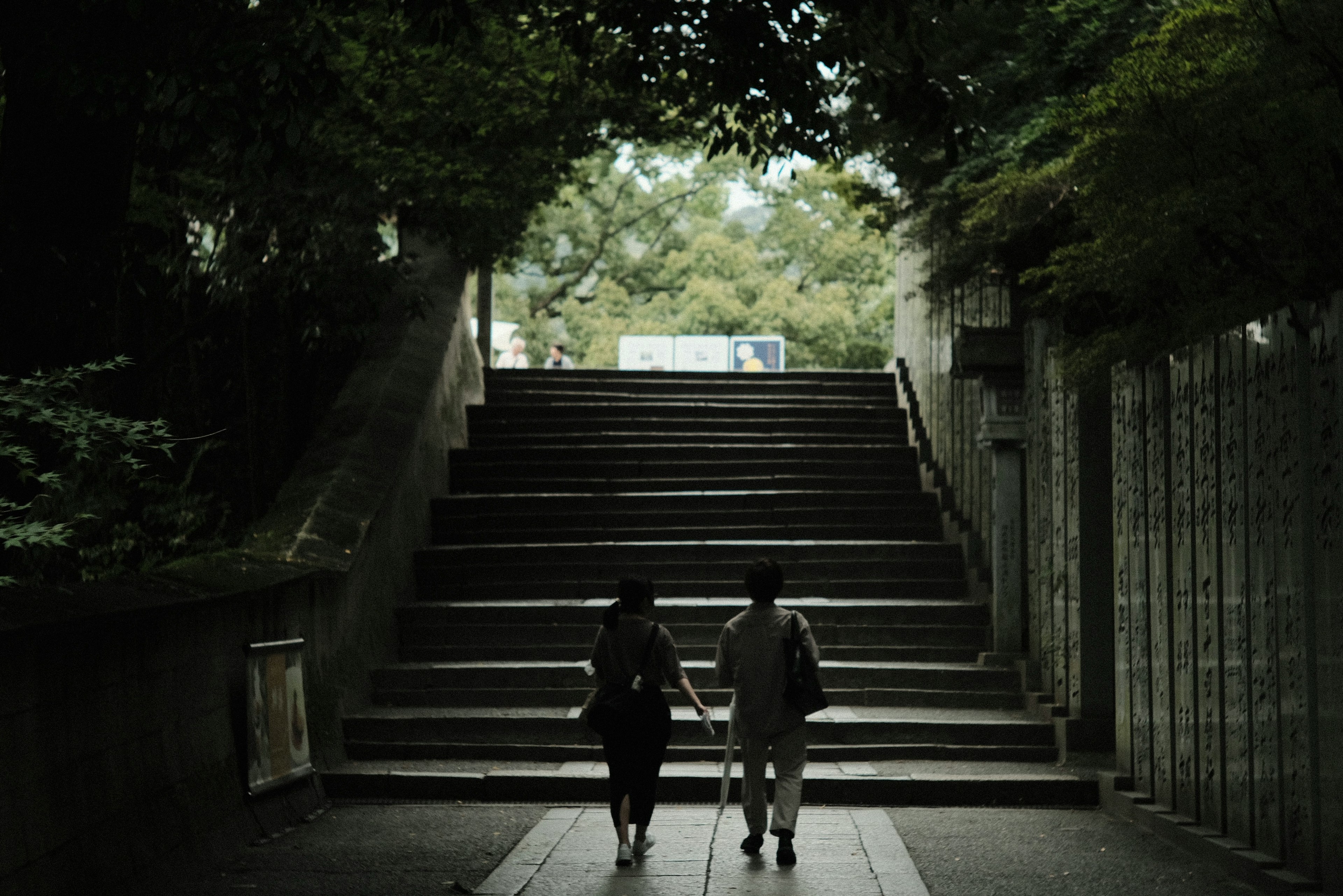 木々に囲まれた階段を上る二人の人物