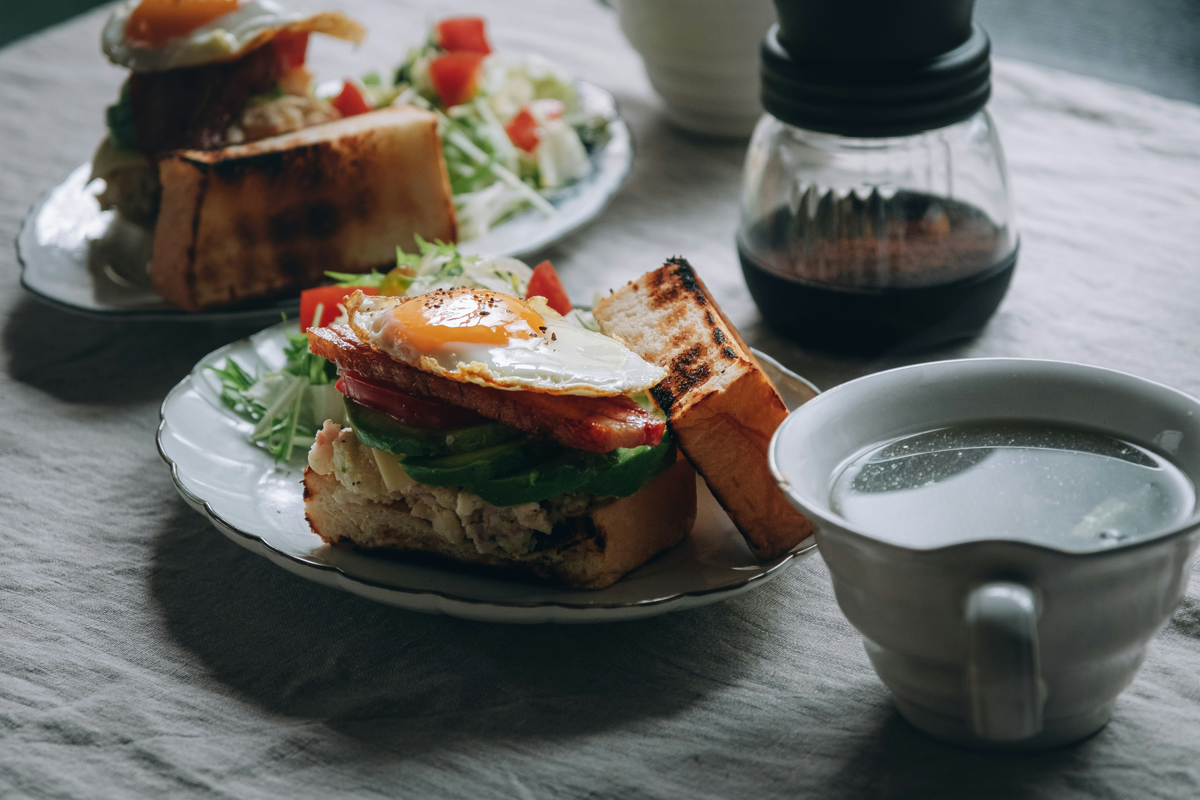 Breakfast scene with a sandwich topped with egg and salad alongside a cup of coffee