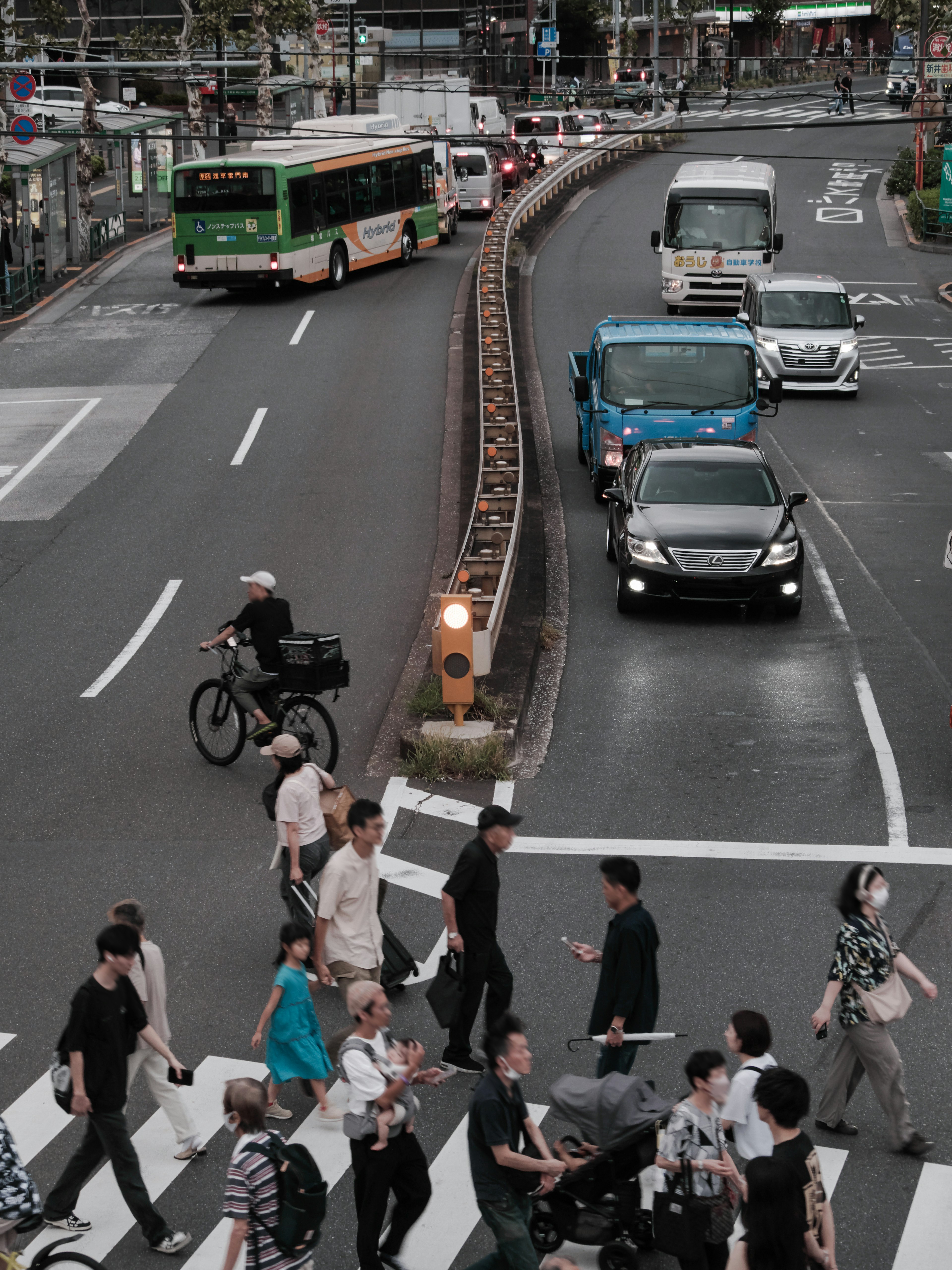 A busy urban intersection with pedestrians crossing the crosswalk and vehicles passing by