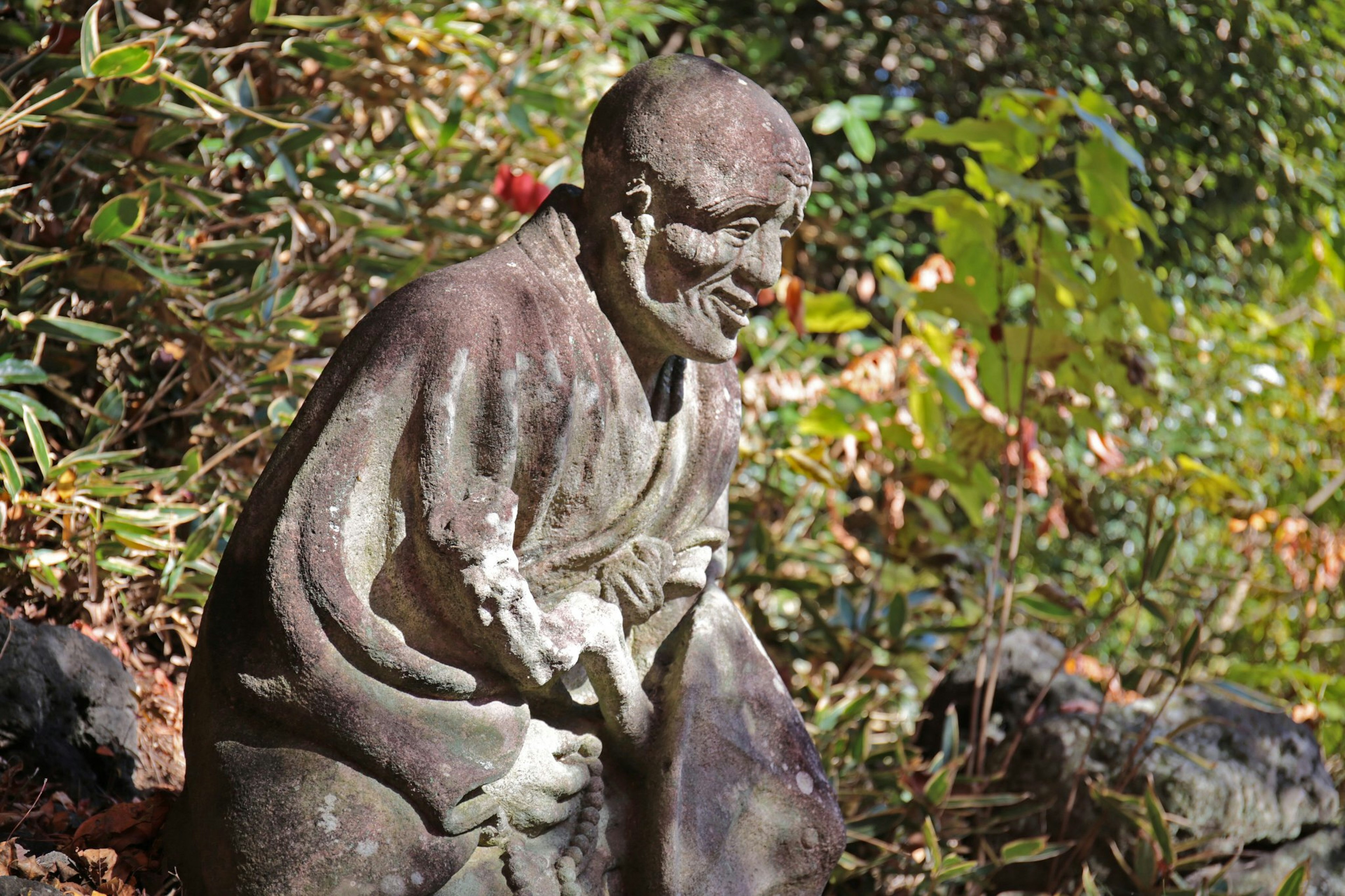 Scultura antica di una figura seduta circondata da vegetazione