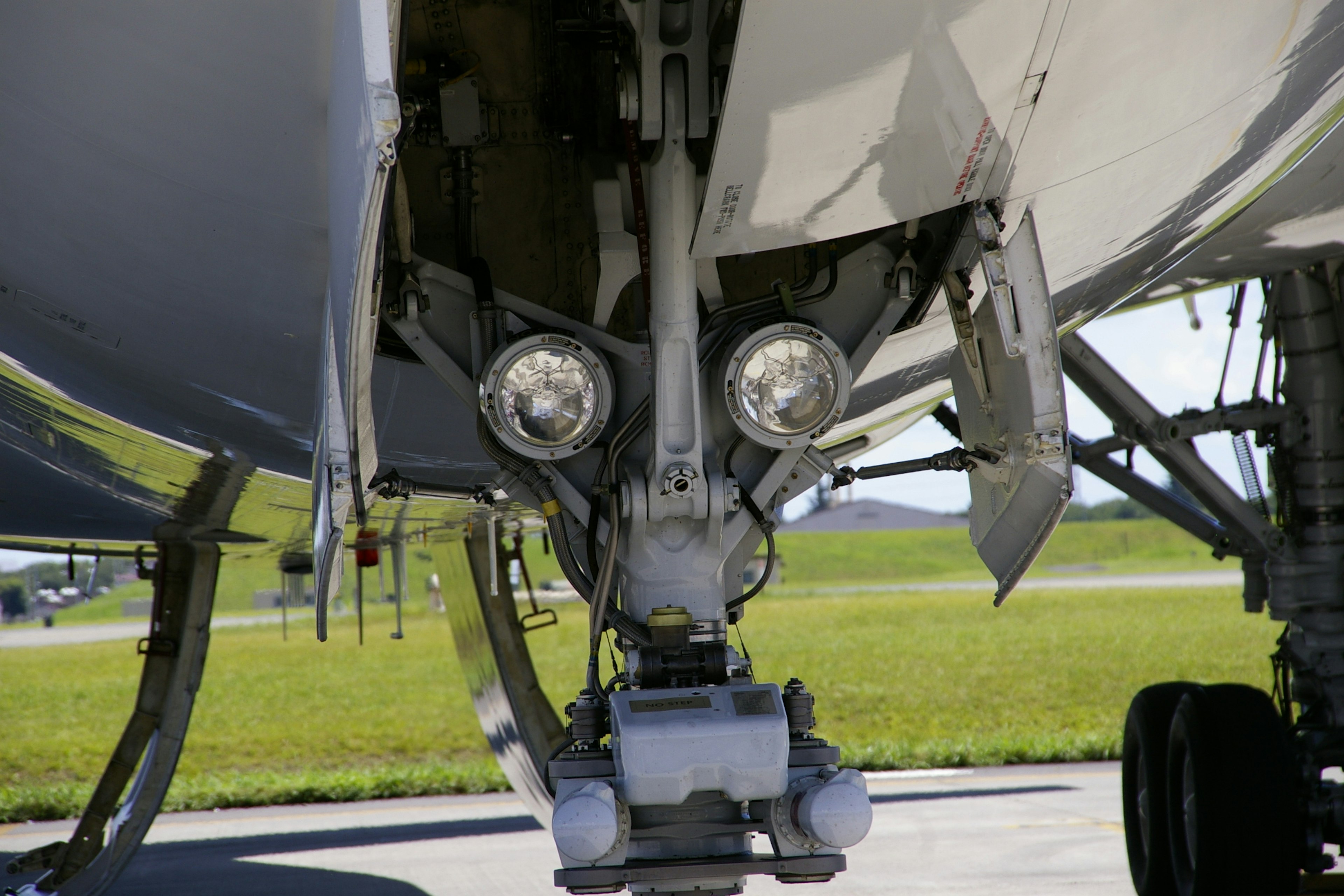 Detailed view of an aircraft's front landing gear with bright lights and grassy background