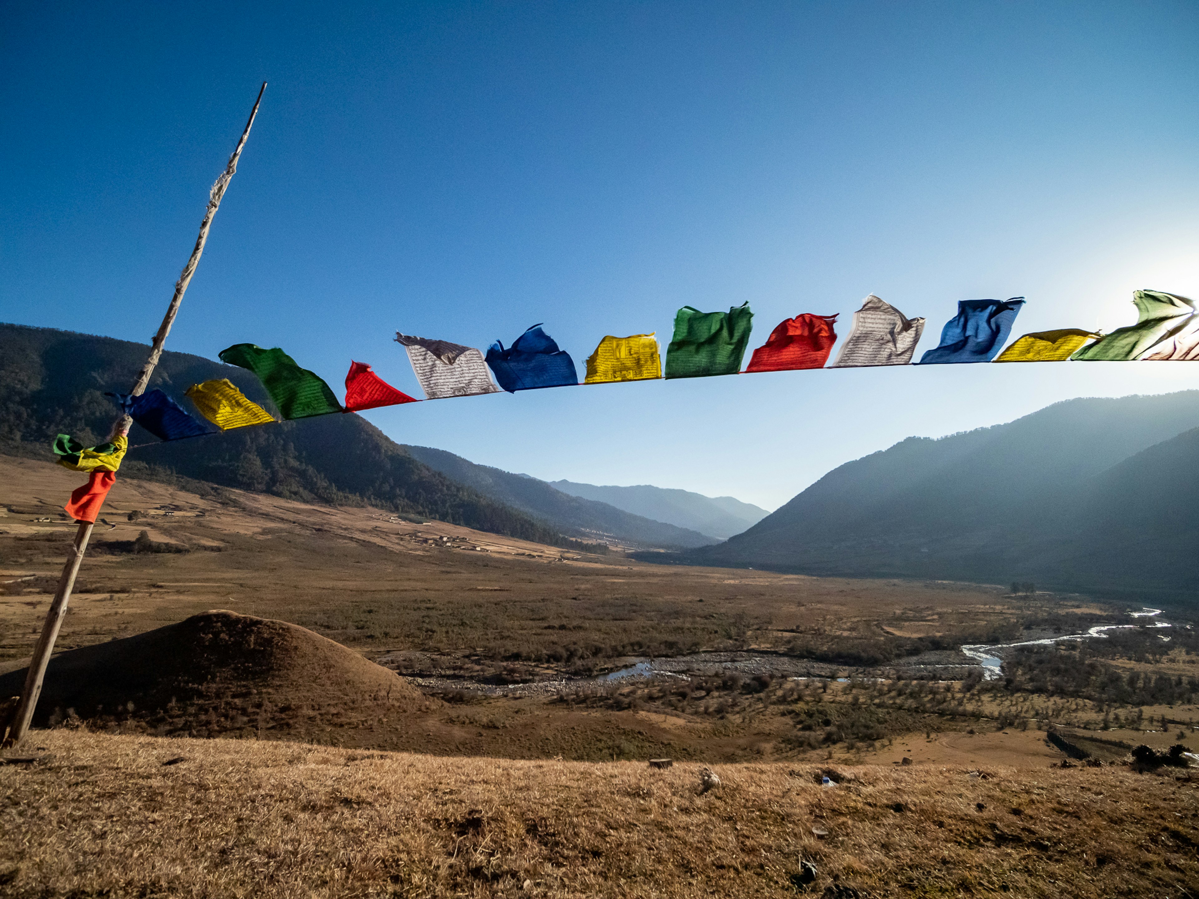 Banderas de oración coloridas ondeando bajo un cielo azul claro sobre un paisaje montañoso