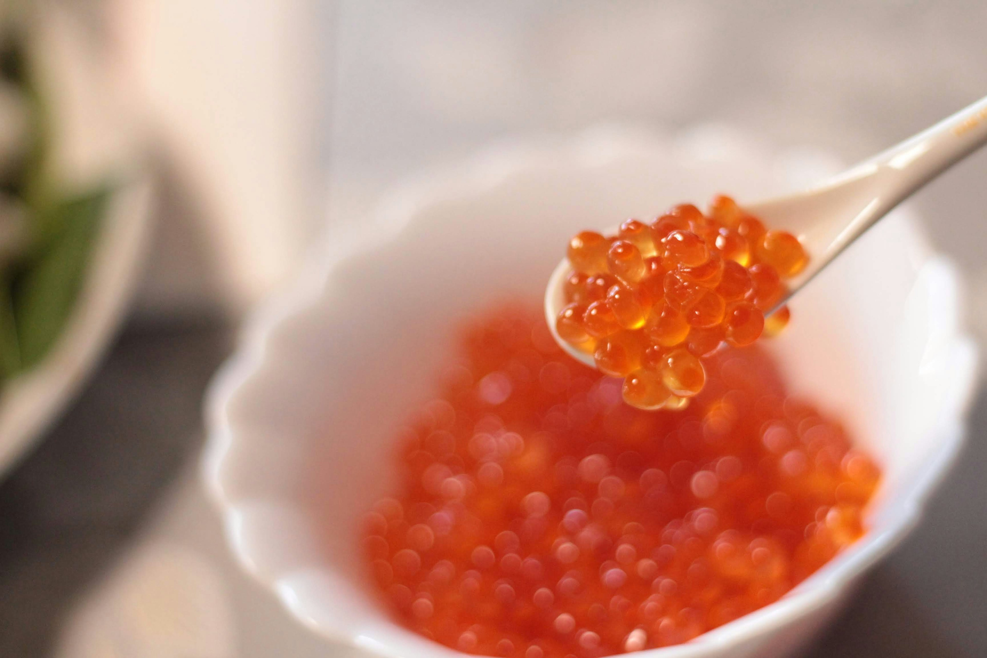 Spoon lifting orange salmon roe from a white bowl