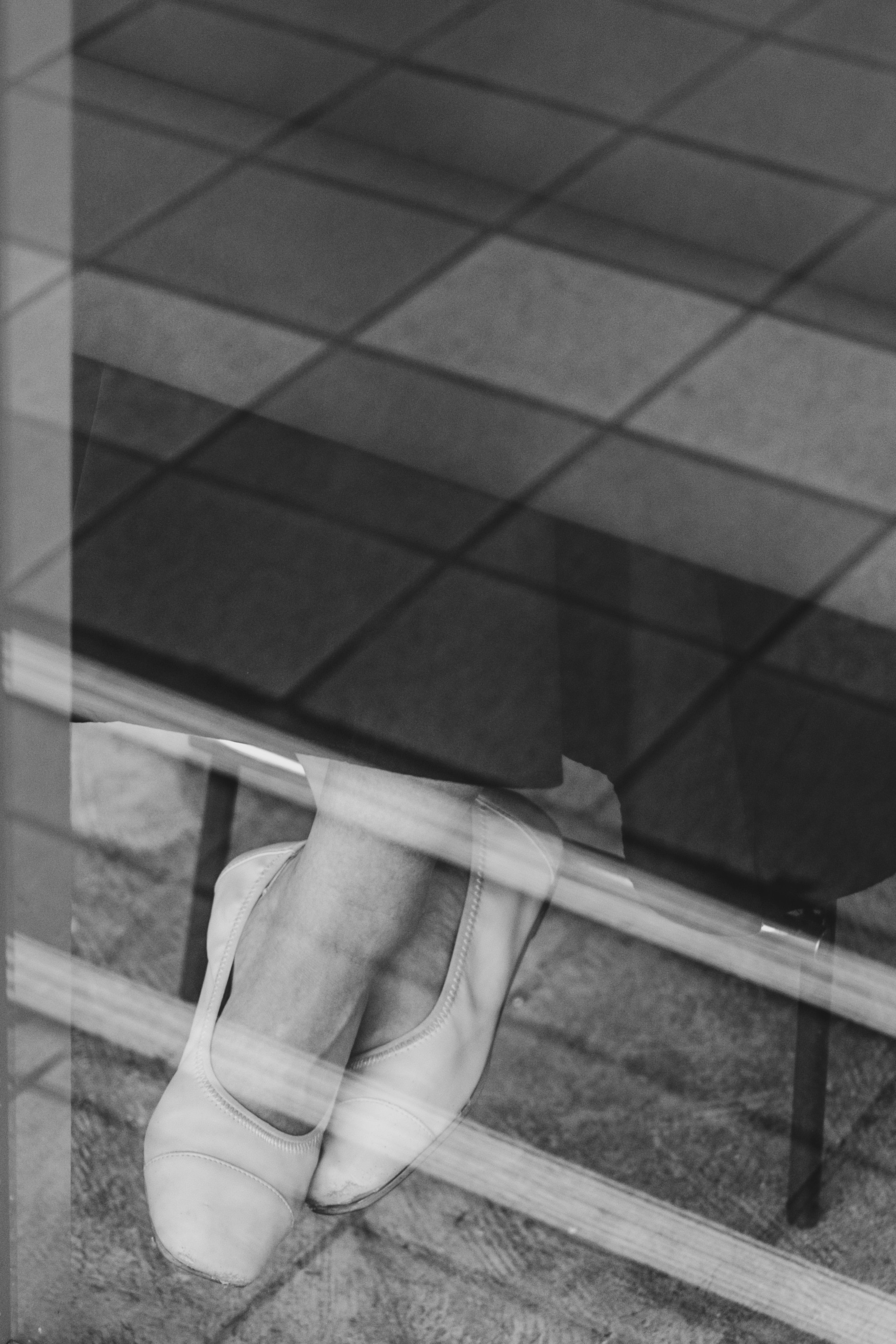 Black and white photo of a foot in white shoes seen through transparent glass