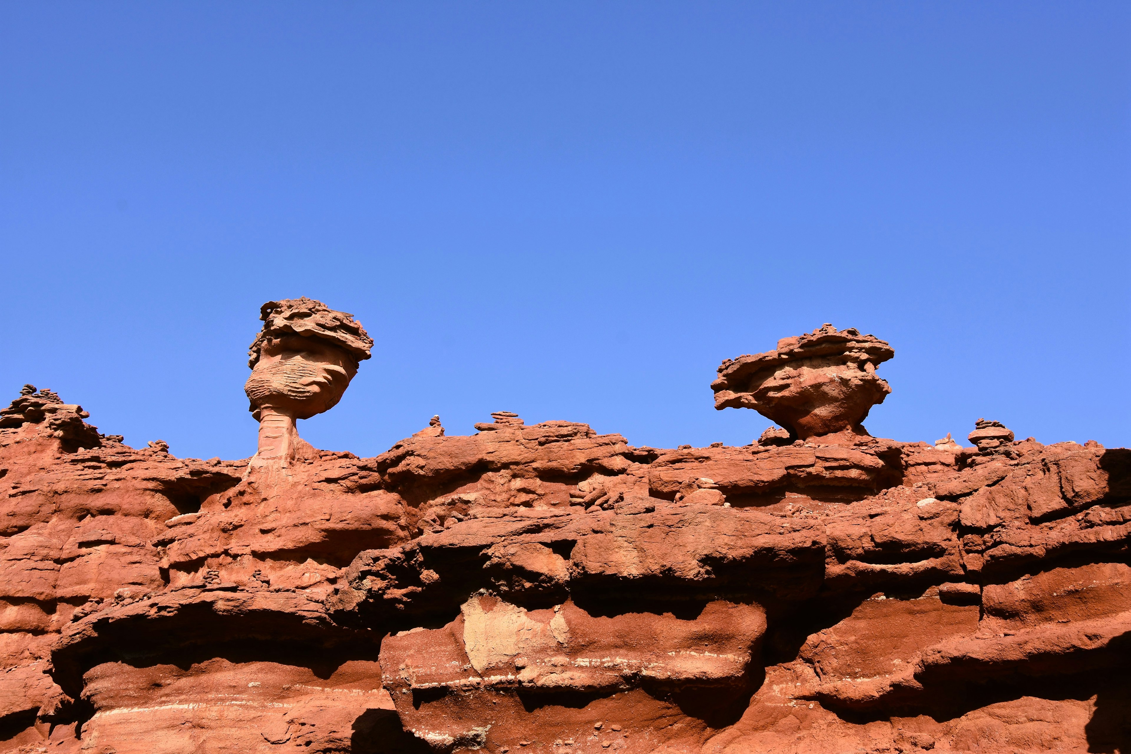 Zwei ungewöhnliche Felsen auf einer roten Klippe vor einem klaren blauen Himmel