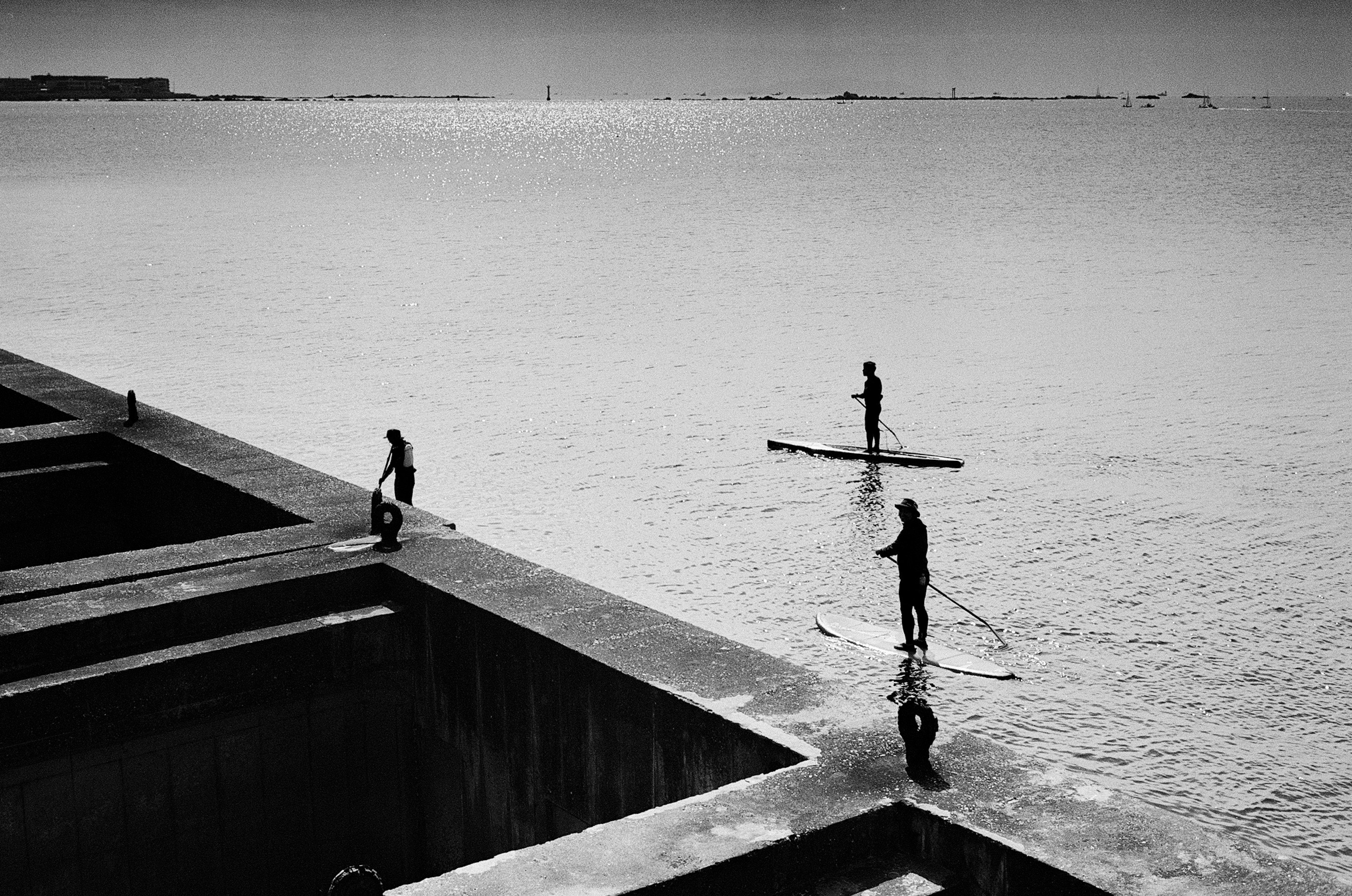 Image en noir et blanc de personnes debout dans la mer près de structures en béton