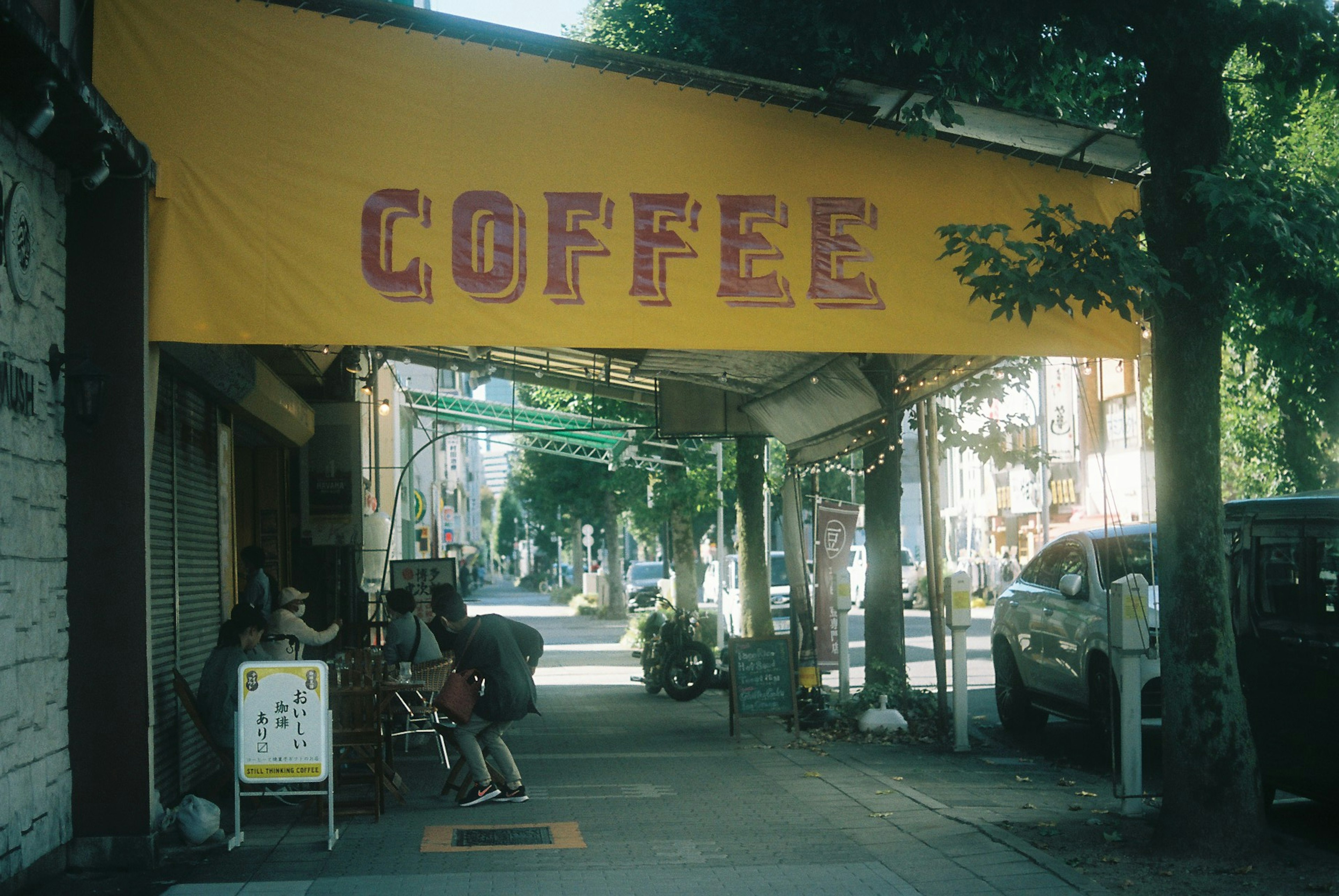 Vista de la calle con un letrero de café y personas sentadas afuera