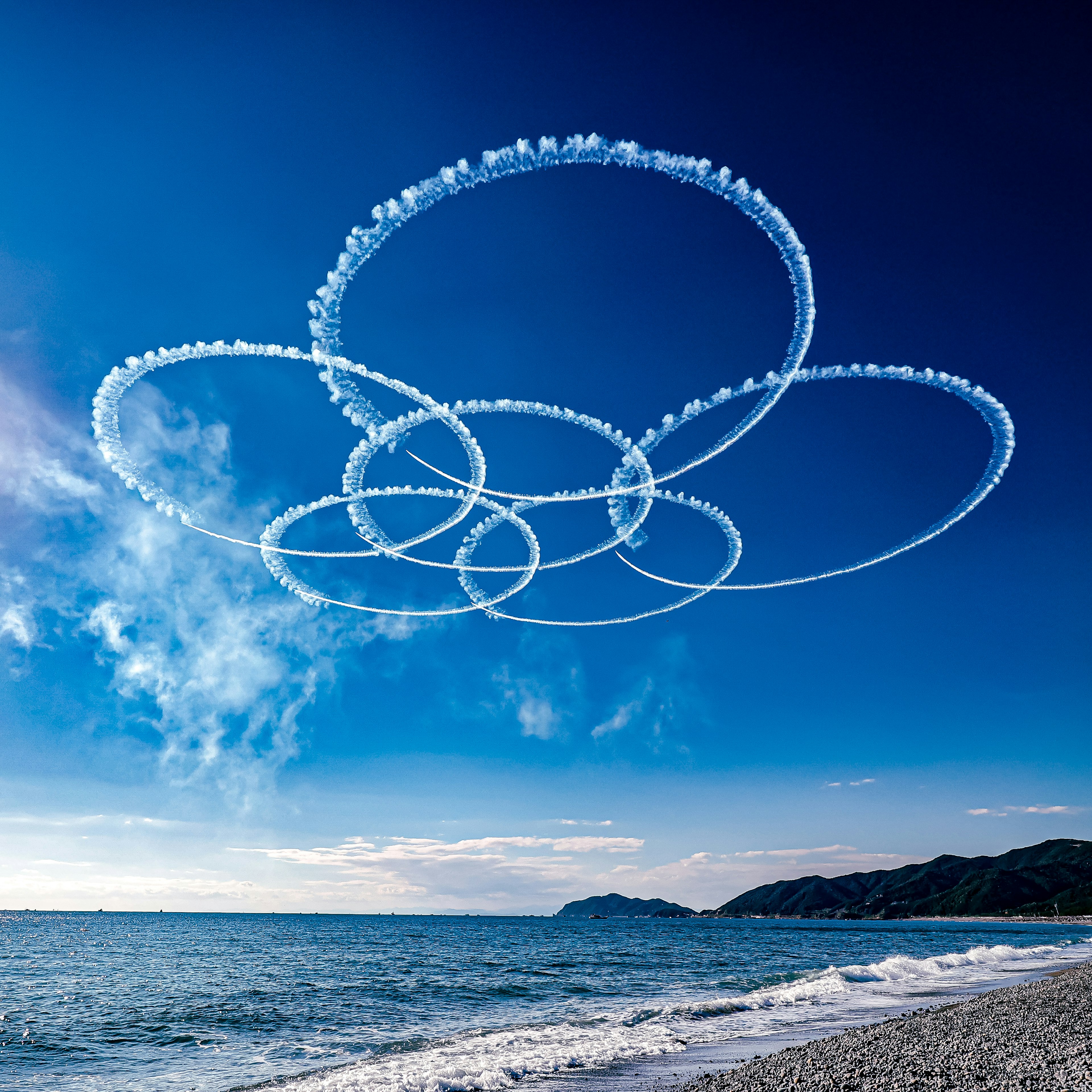 青い空に描かれた白い煙の輪と海岸の風景