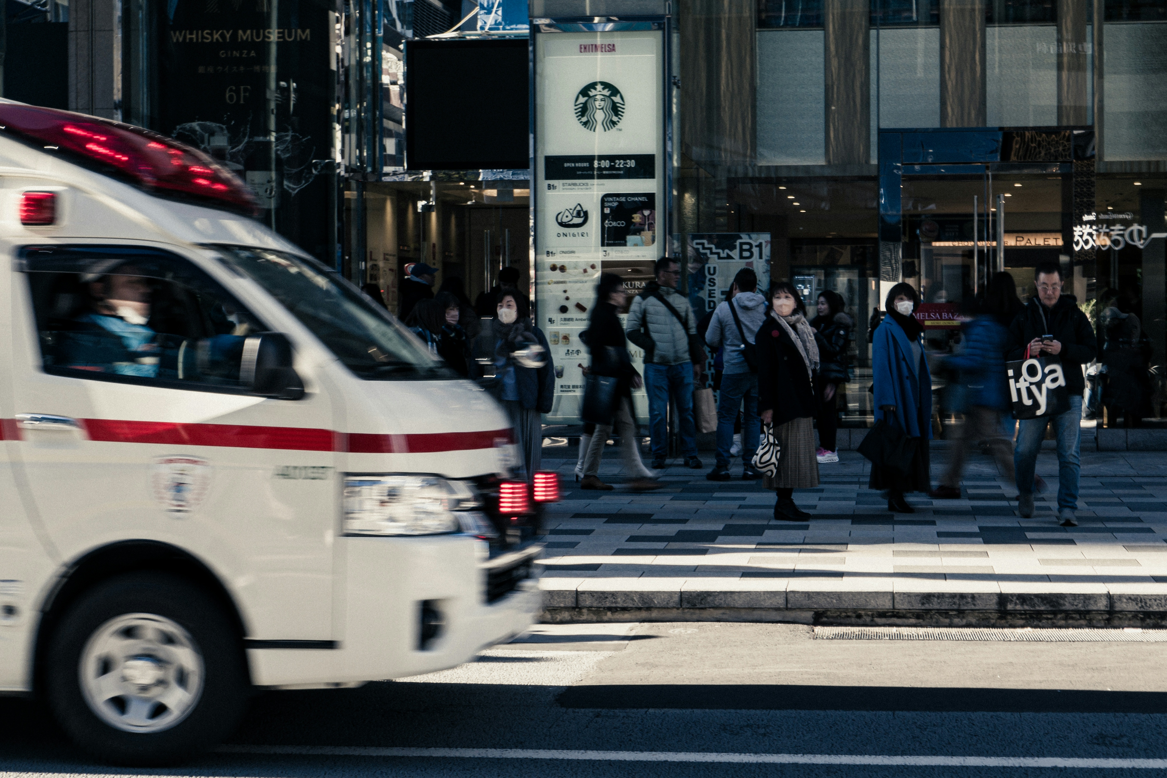 人々が通りを横断する中を走る救急車の画像