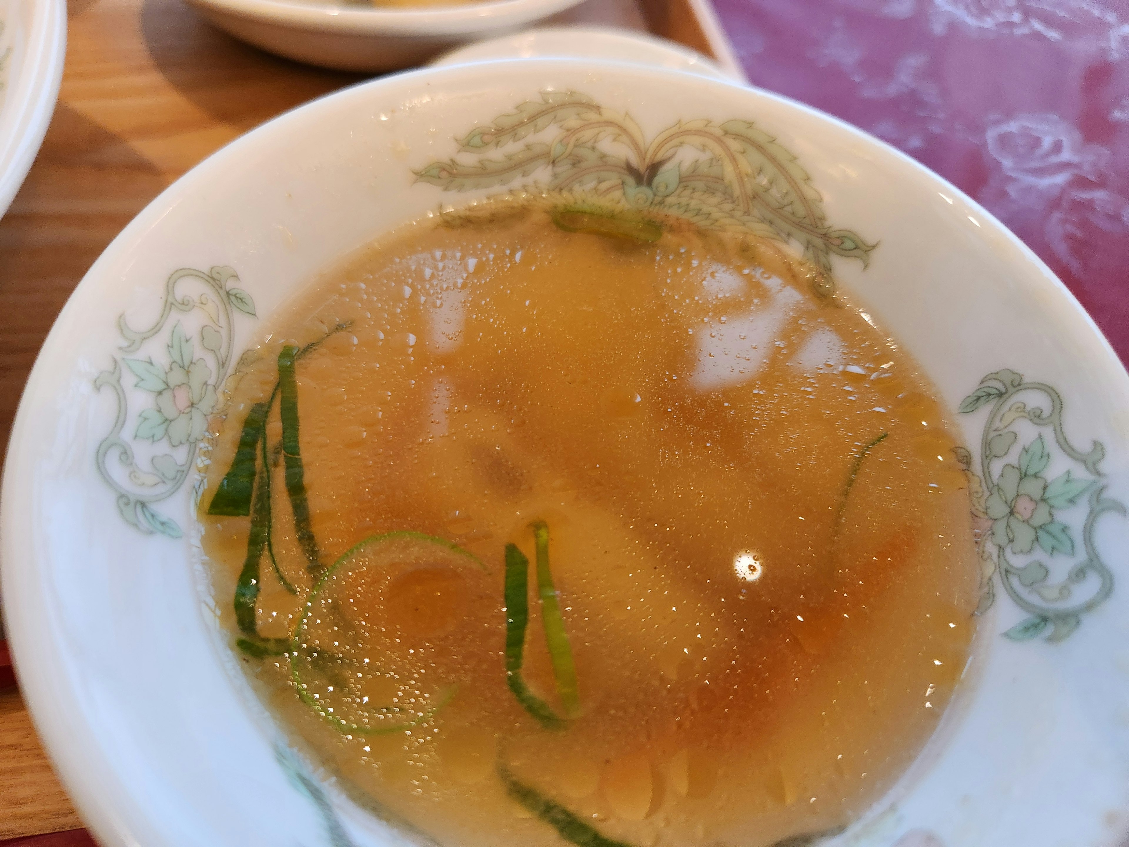 Caldo claro con hierbas verdes finas en un tazón blanco