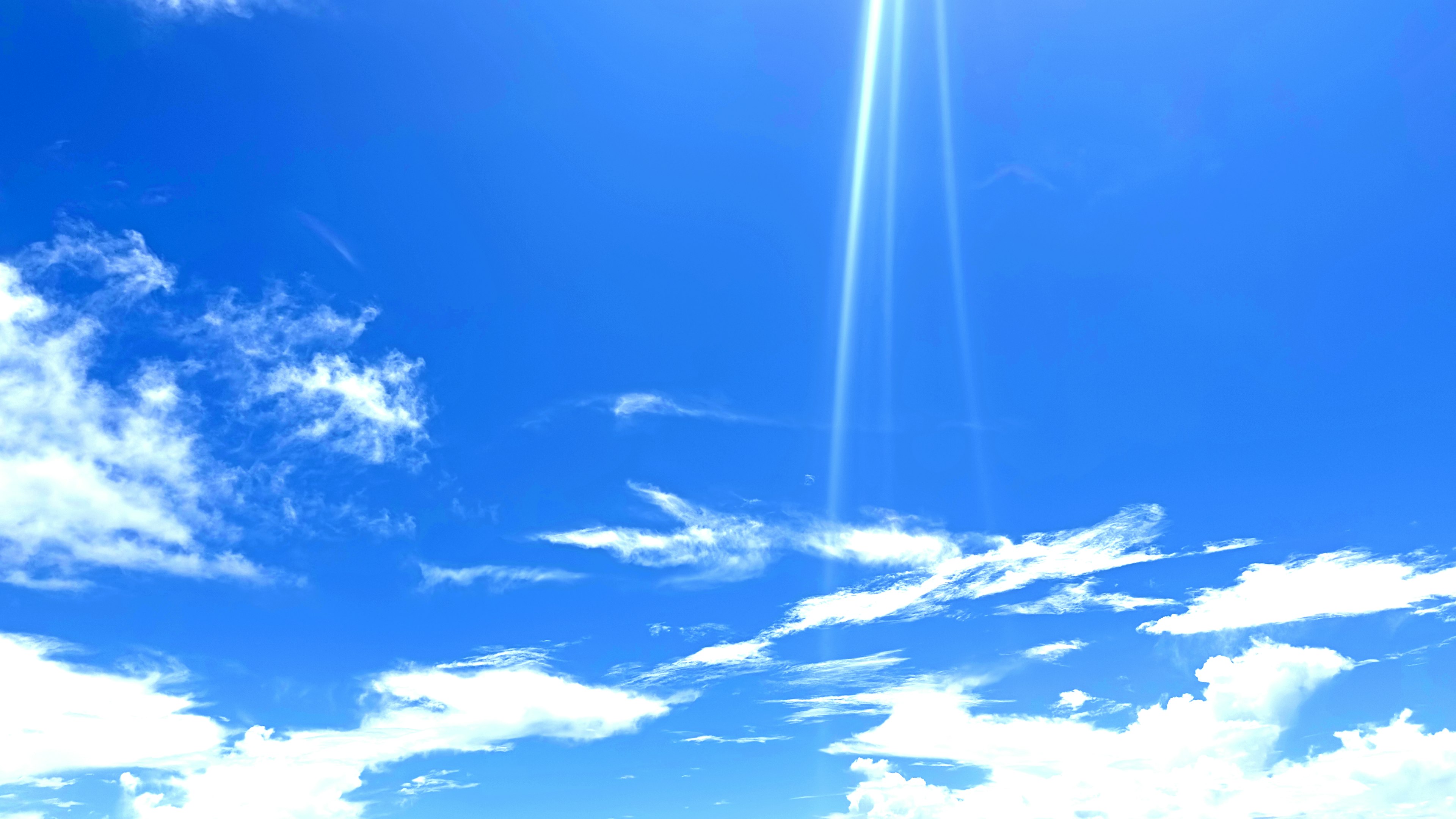 青空に白い雲と太陽の光が差し込む風景