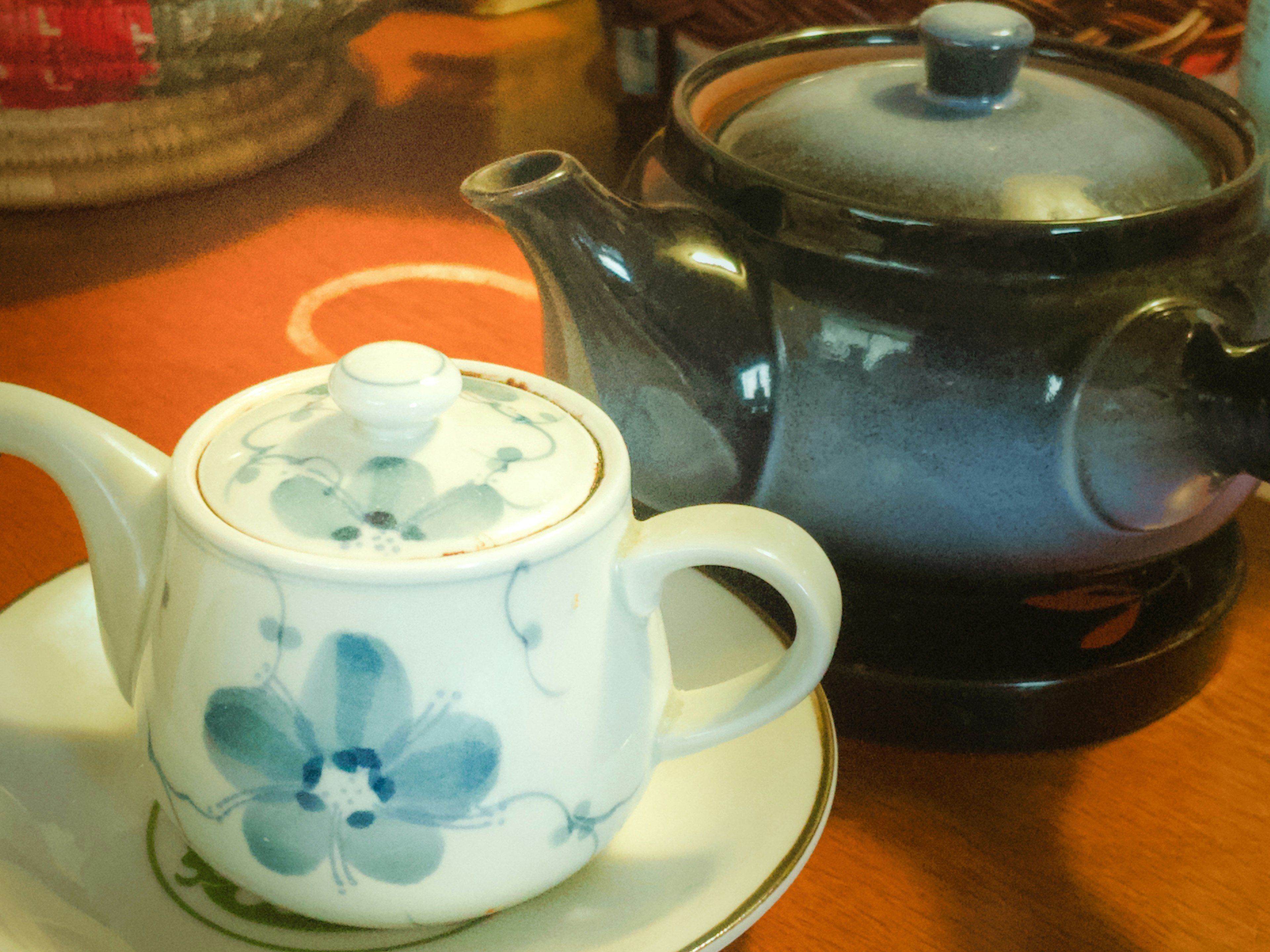 Una tetera azul con flores y una tetera negra sobre una mesa de madera