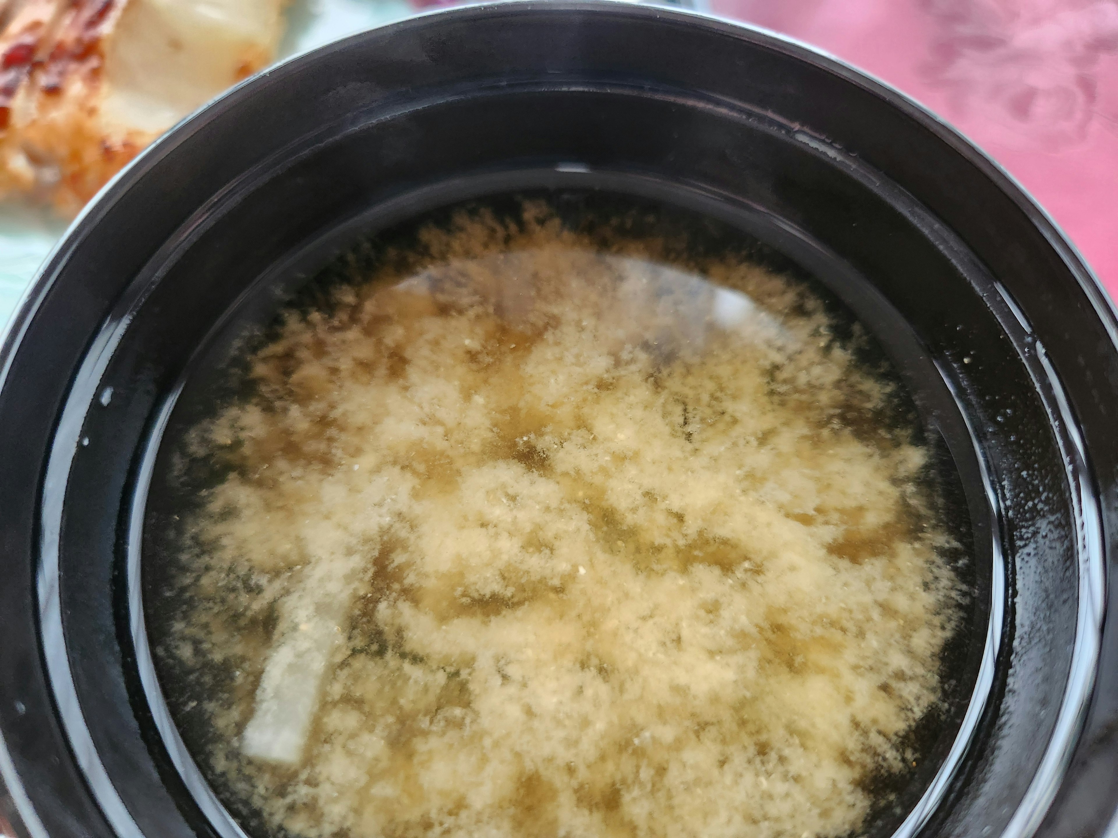 Miso-Suppe in einer schwarzen Schüssel mit schaumiger Oberfläche