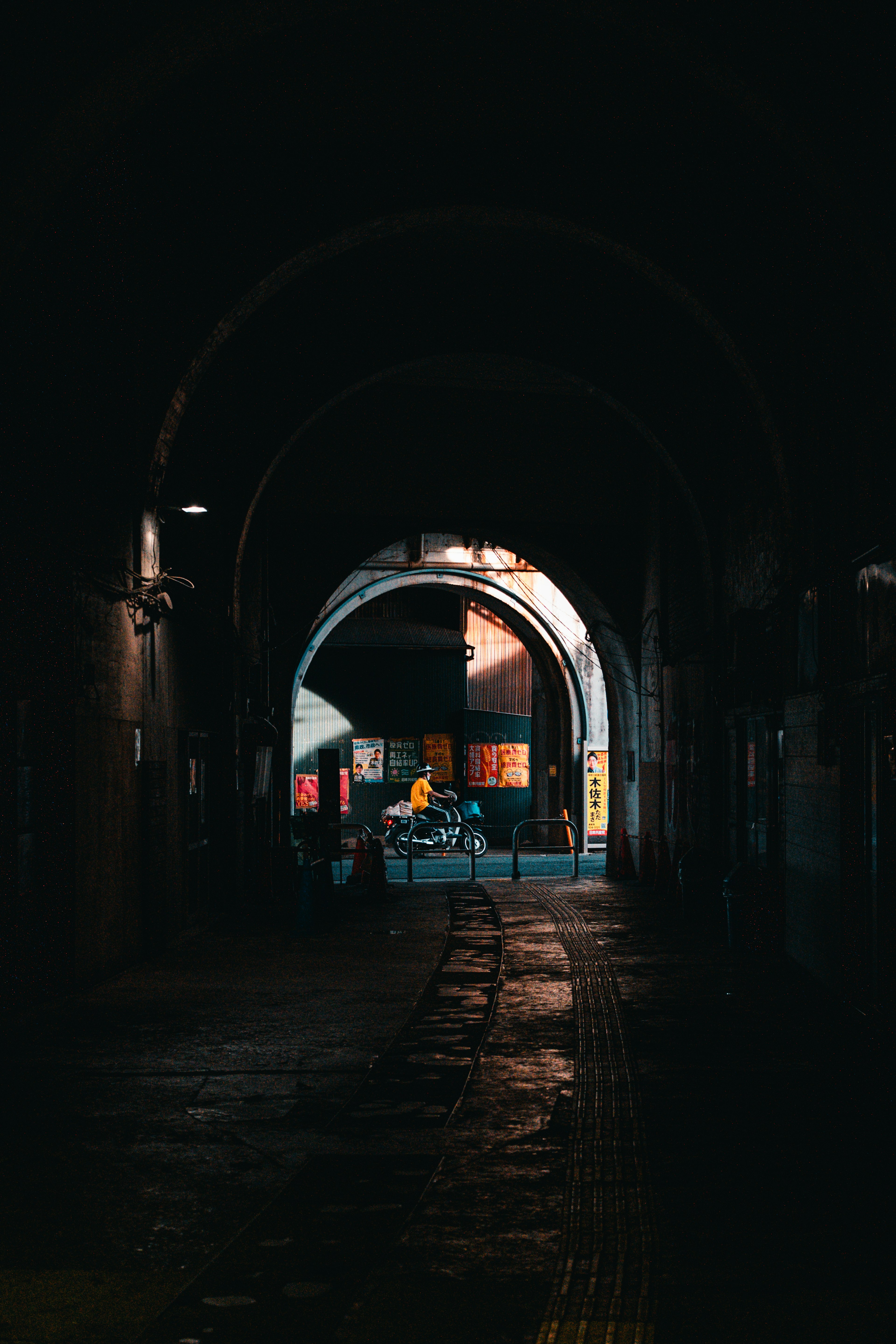 Dark arched corridor with light streaming in and a distant figure