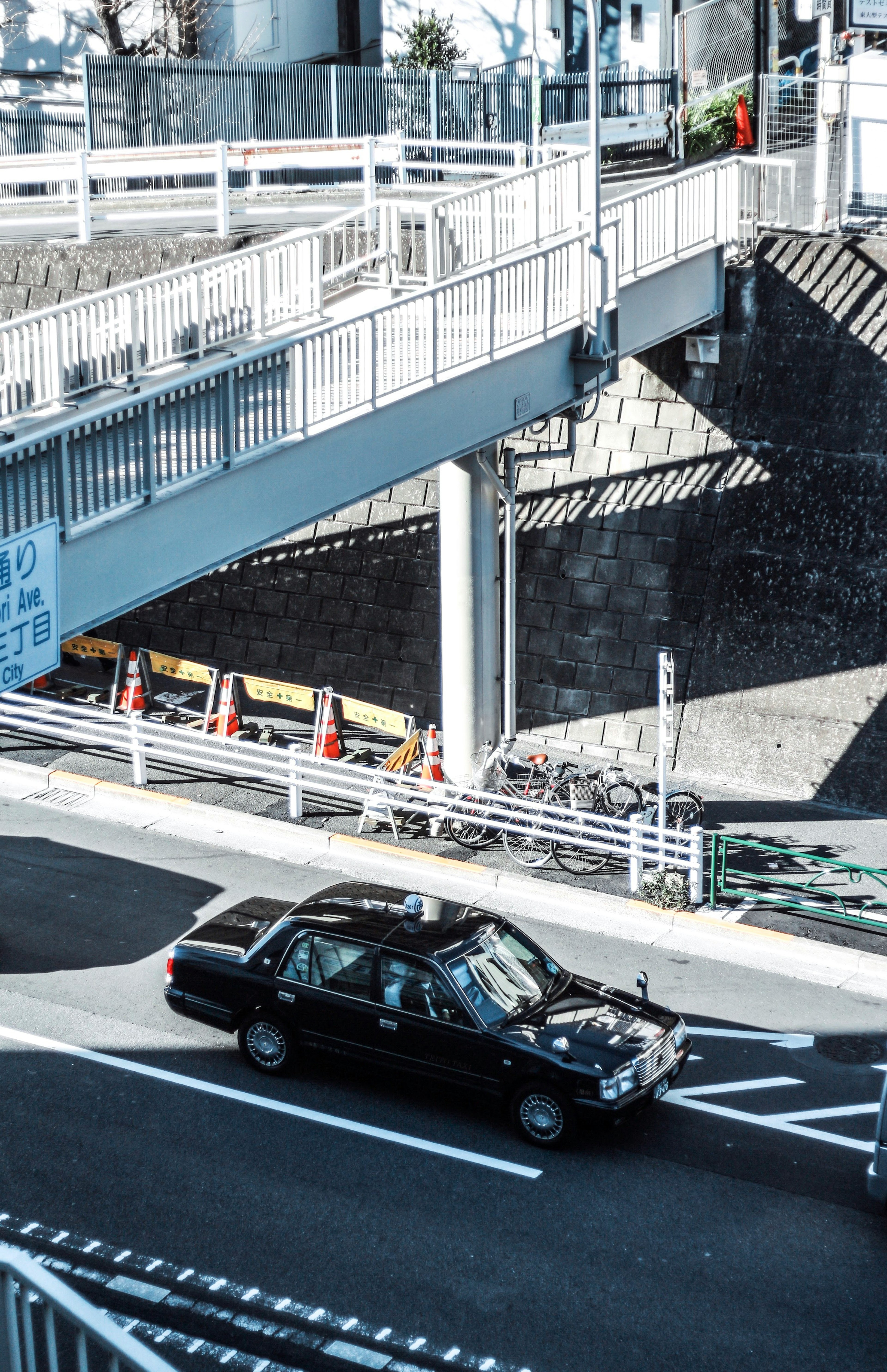 黒い車が横断歩道の近くを走っている写真 橋の下にある構造物と影のパターンが見える