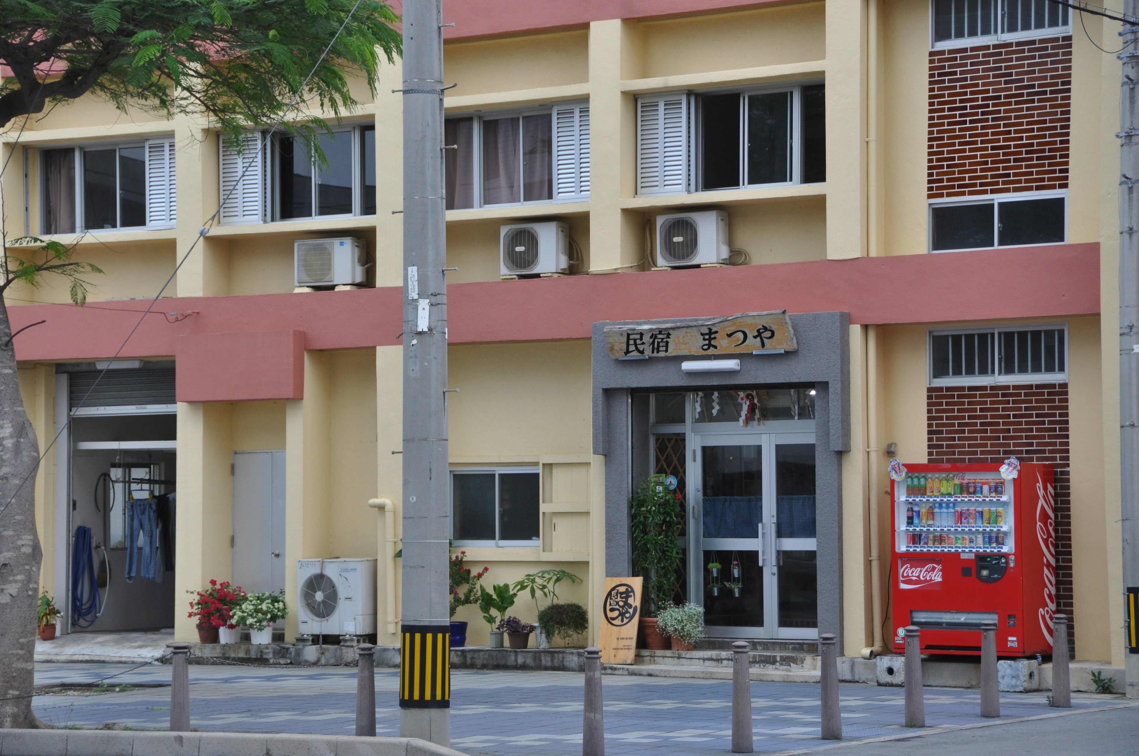 Fachada de un edificio comercial con unidades de aire acondicionado en las ventanas flores coloridas en un pequeño jardín