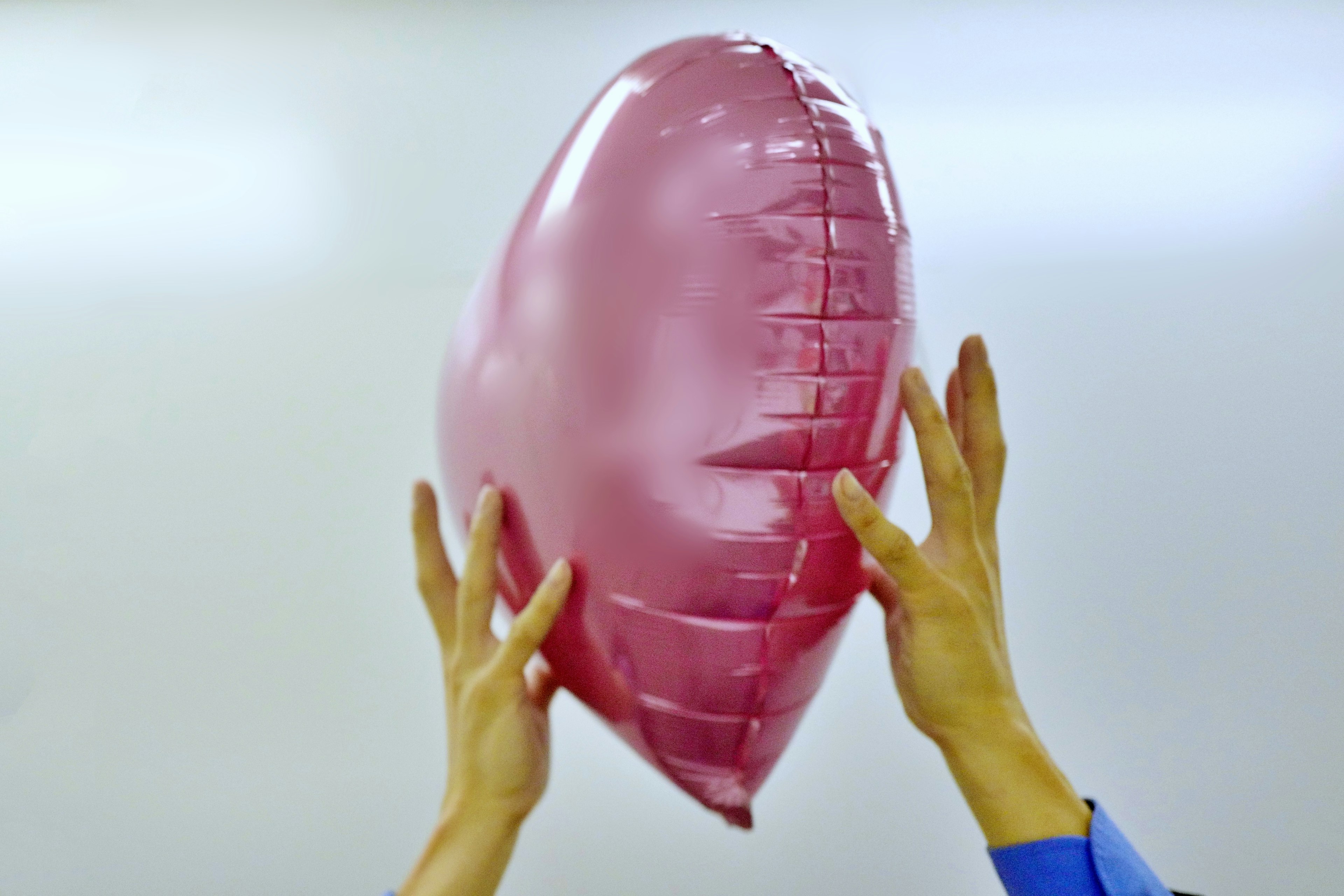 Hands holding a pink heart-shaped balloon