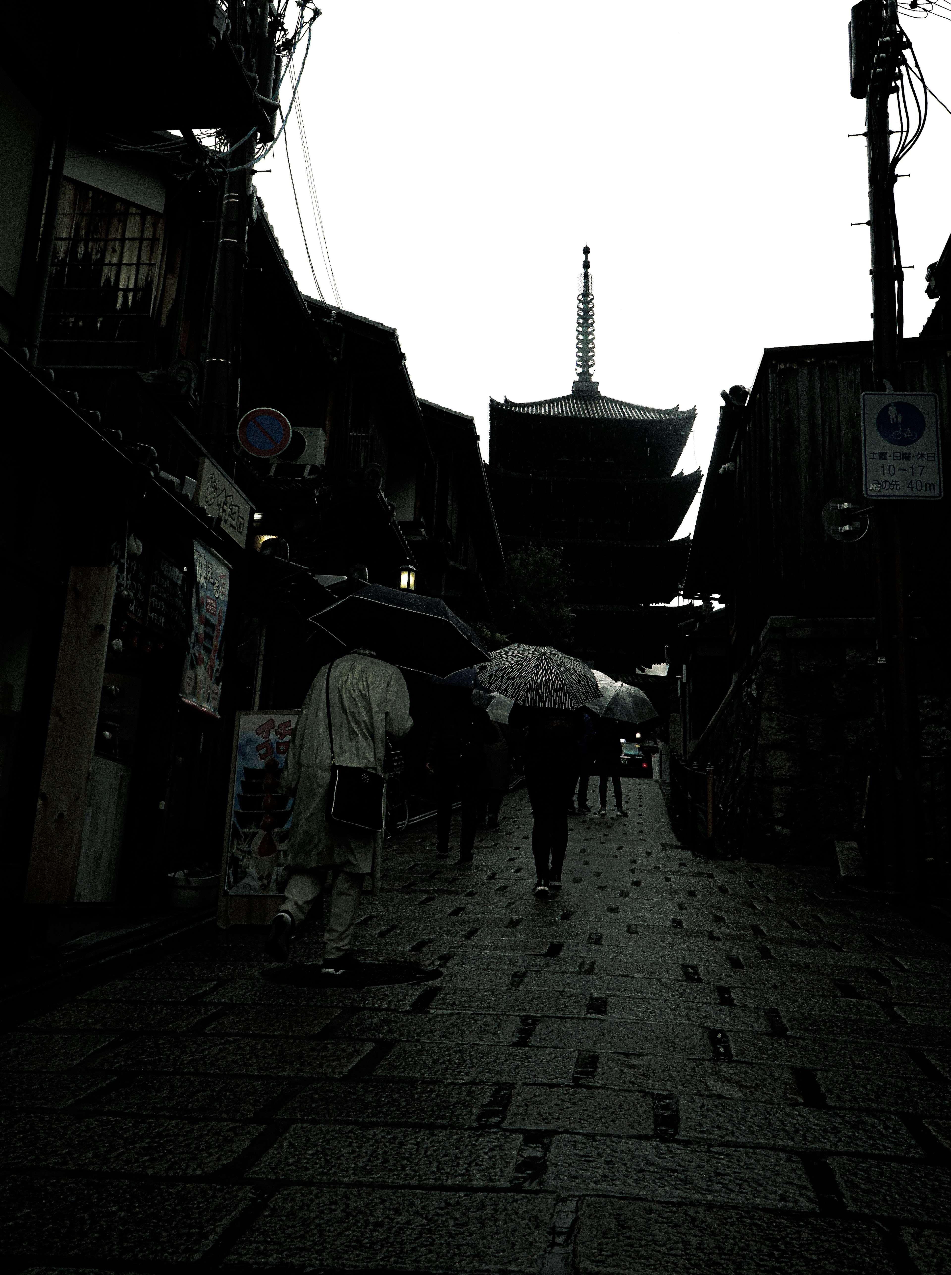 雨の中で傘をさした人々が歩いている古い街並みと寺