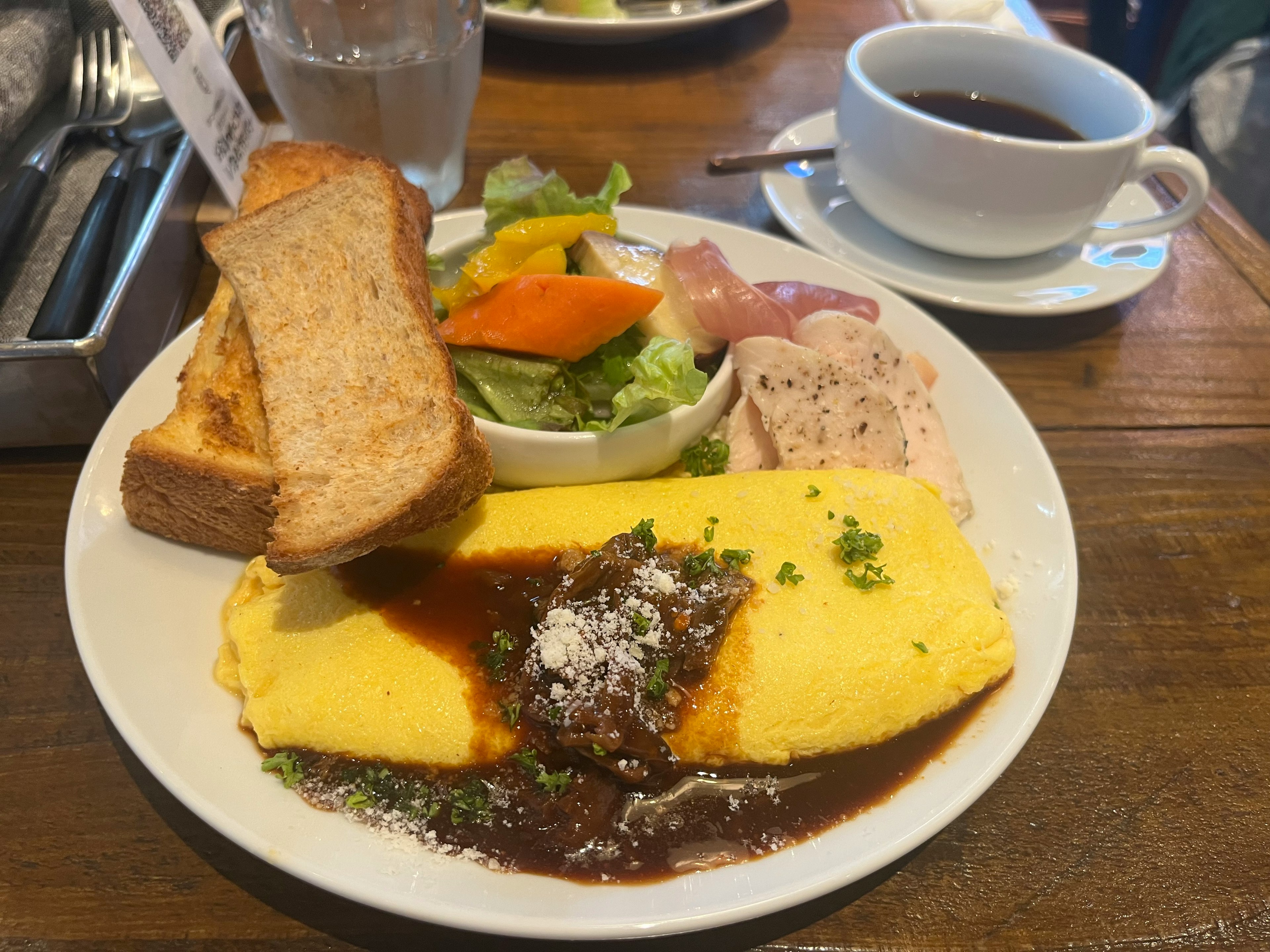 Piring sarapan dengan omelet, salad, roti panggang, dan kopi