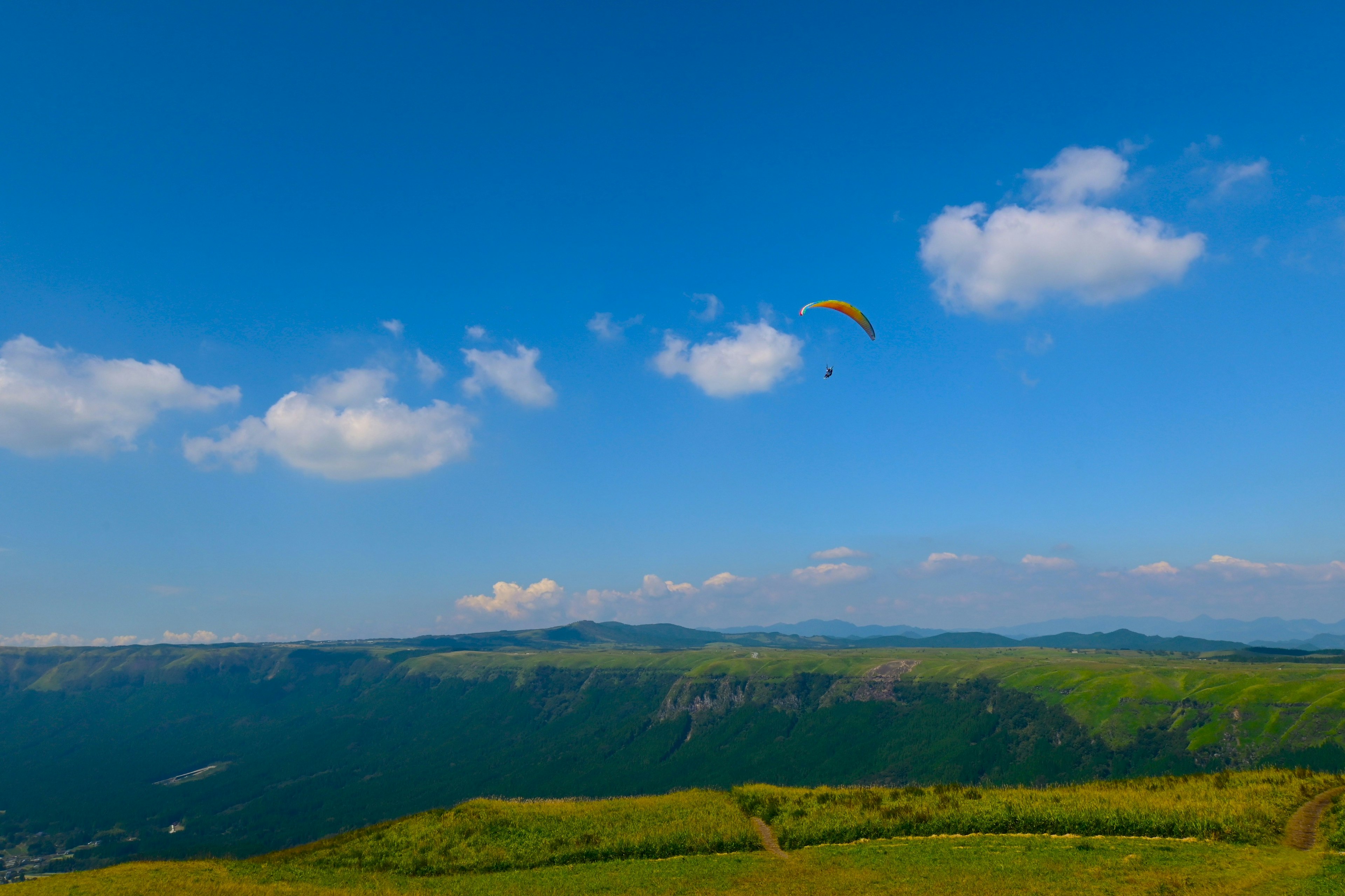 Green hills under a blue sky with a paraglider