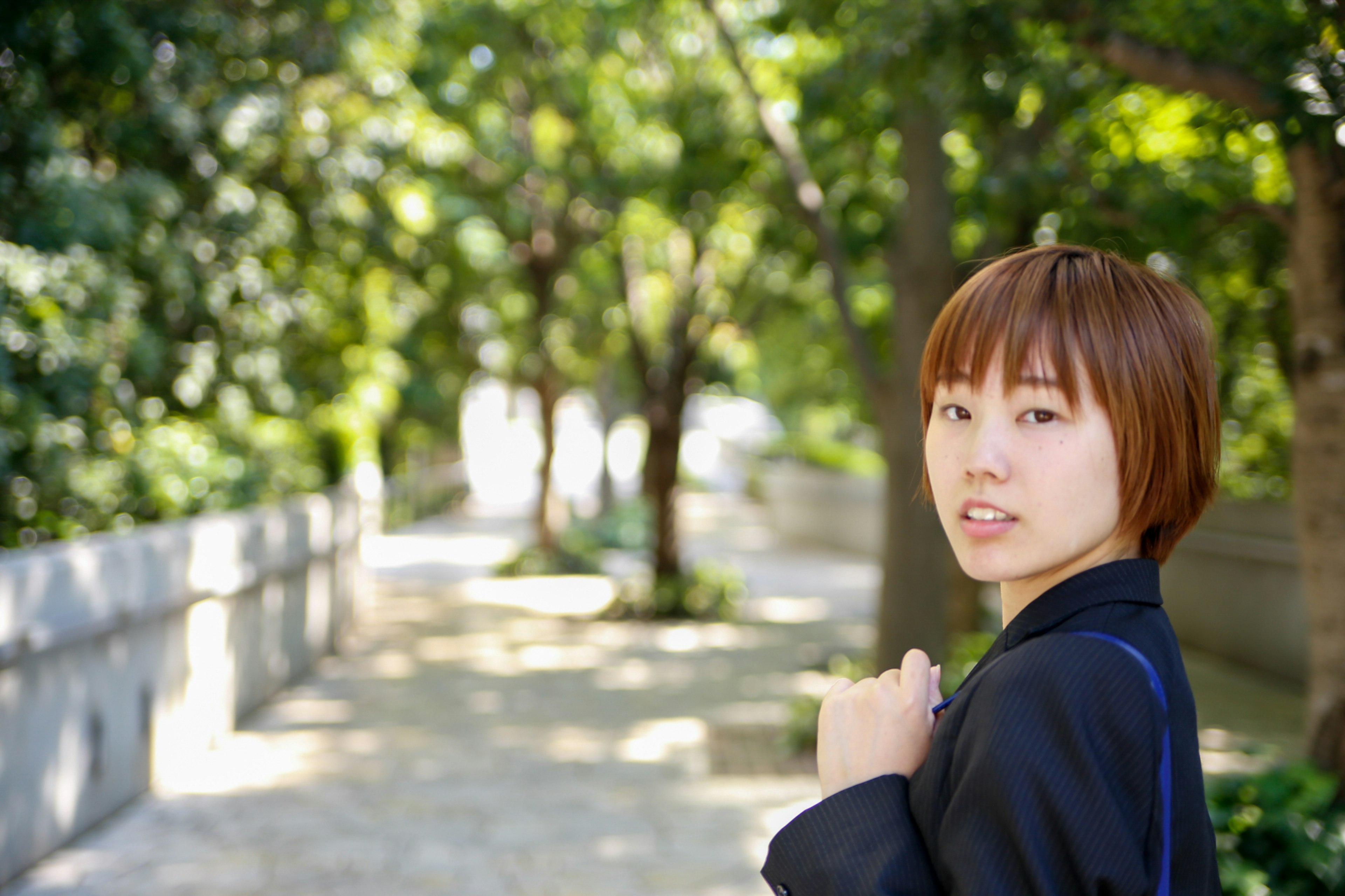 A short-haired woman looking back on a tree-lined path