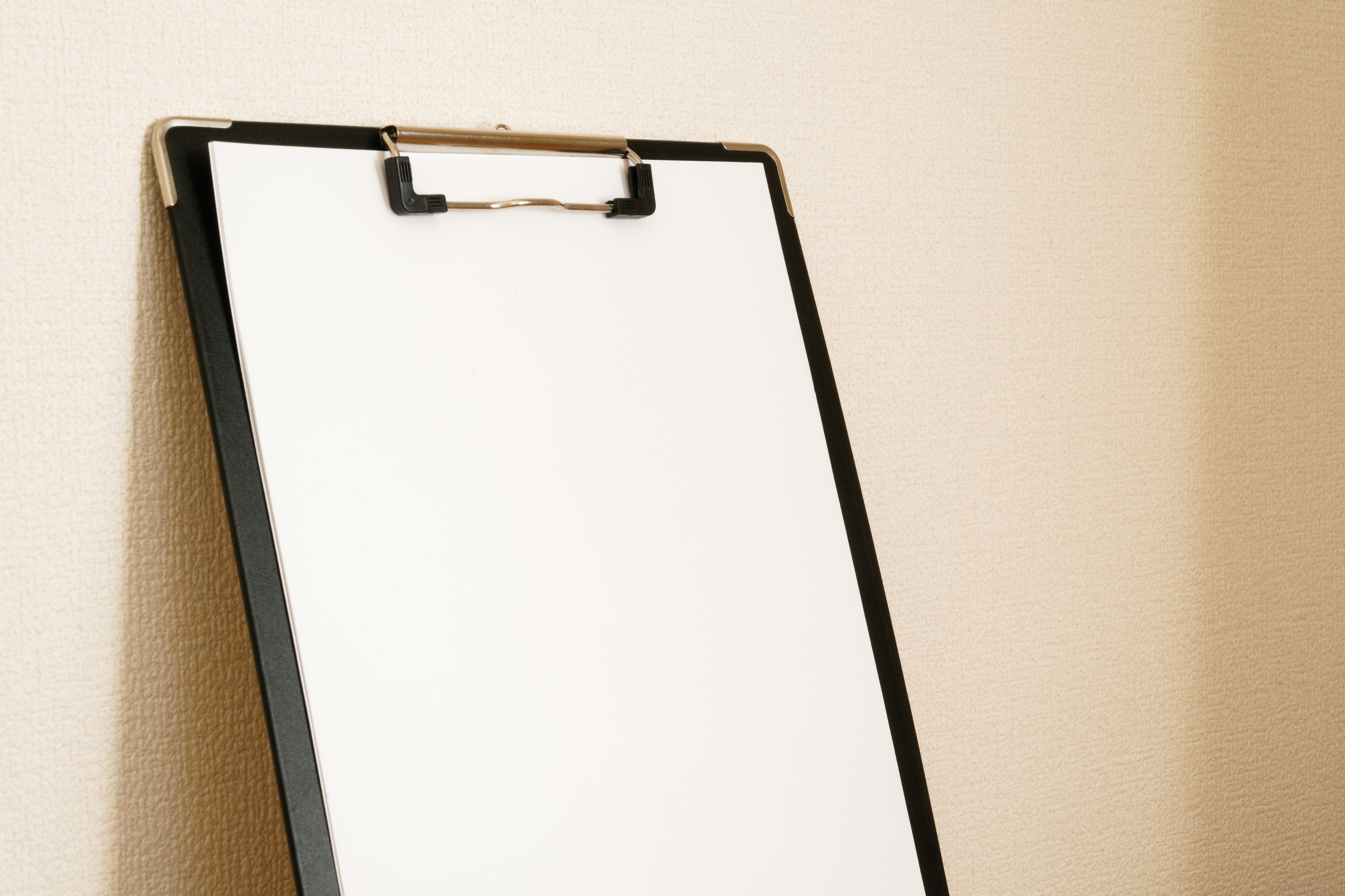 A blank whiteboard on a black clipboard against a neutral wall