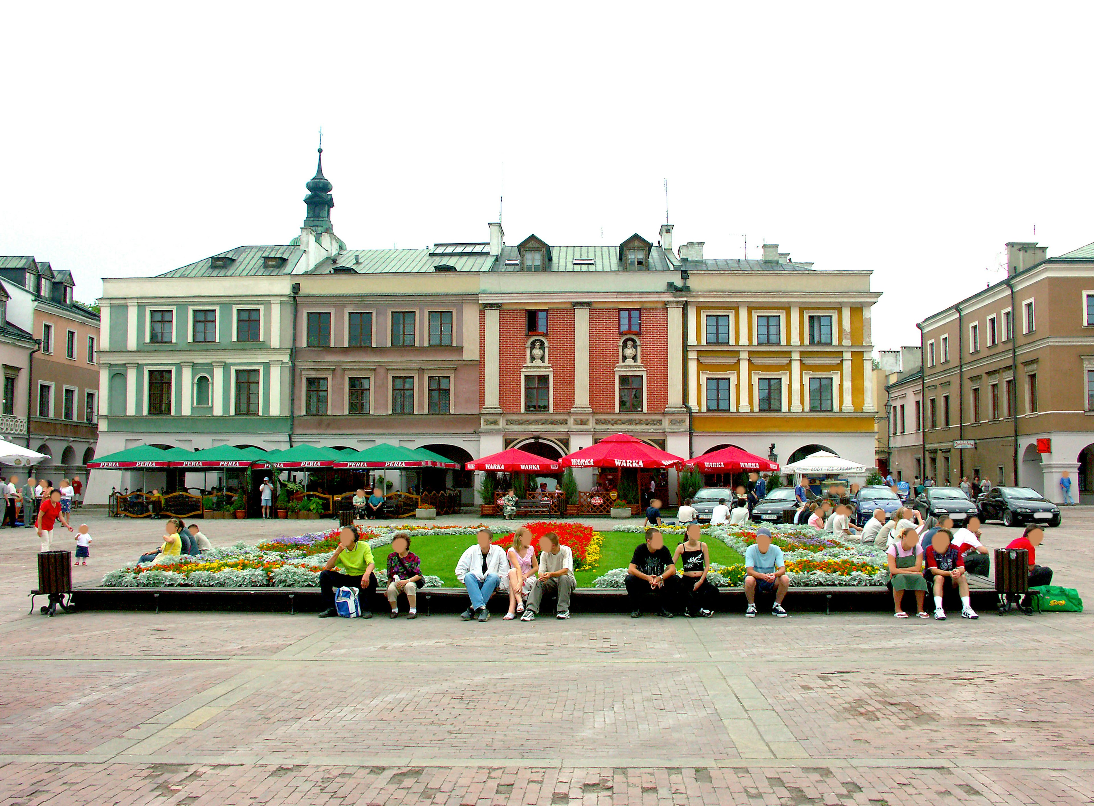 People sitting in a plaza with colorful tents and buildings