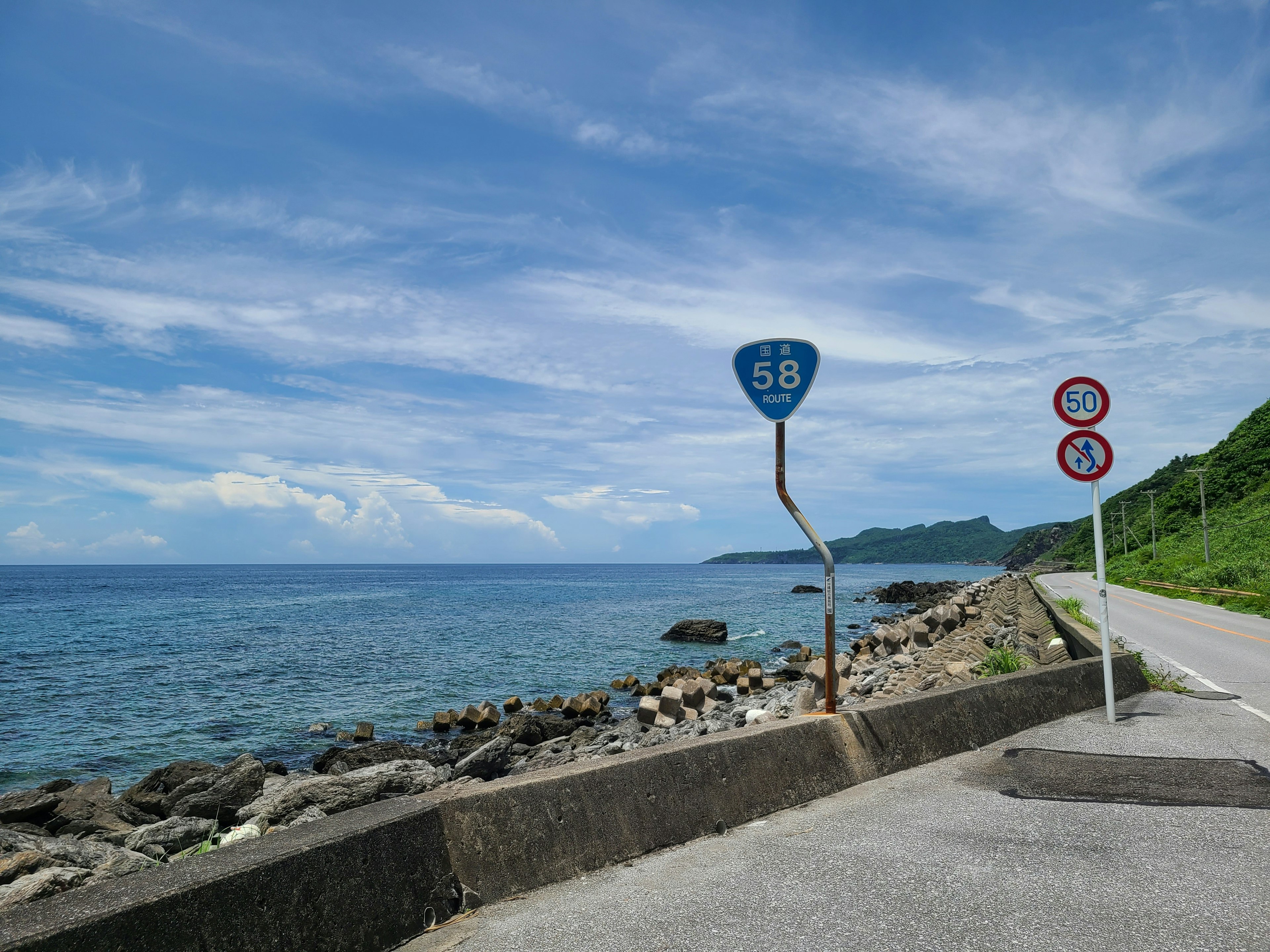 Route côtière avec ciel bleu et vue sur l'océan présentant des panneaux de signalisation et des rochers