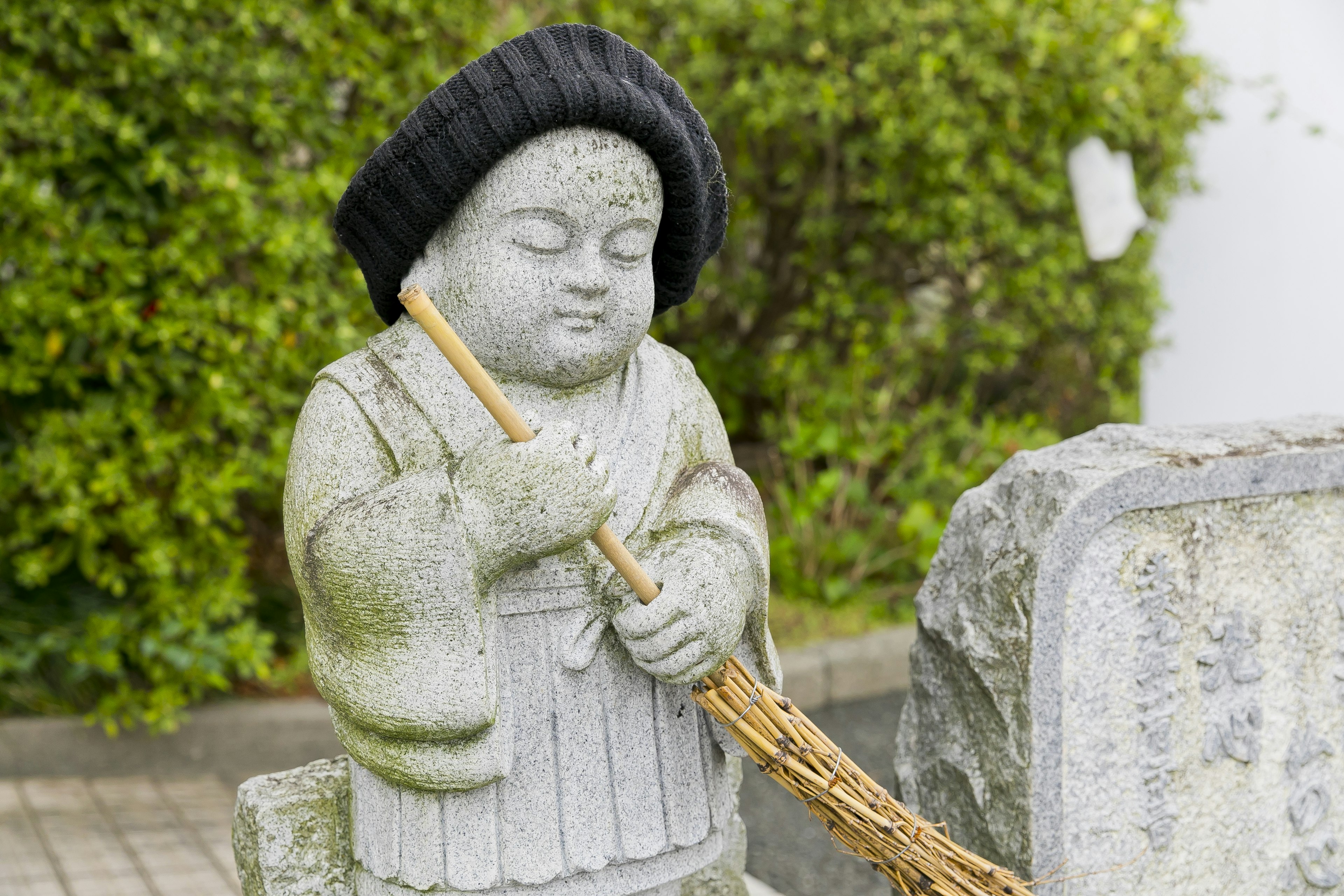 Una estatua de piedra de un niño sosteniendo una escoba con un sombrero negro y un fondo verde