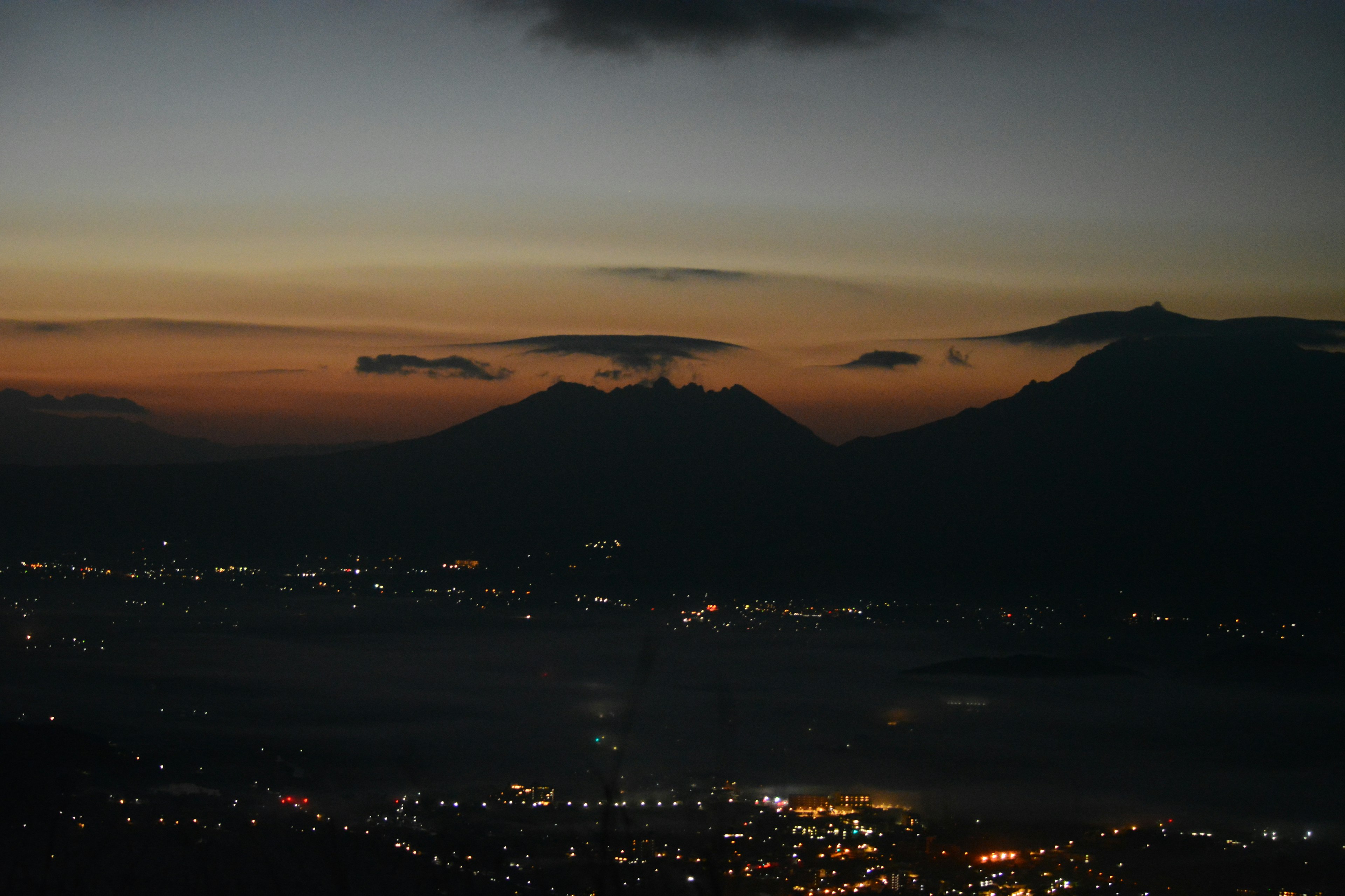 夜明けの山々と都市の光が映る美しい風景