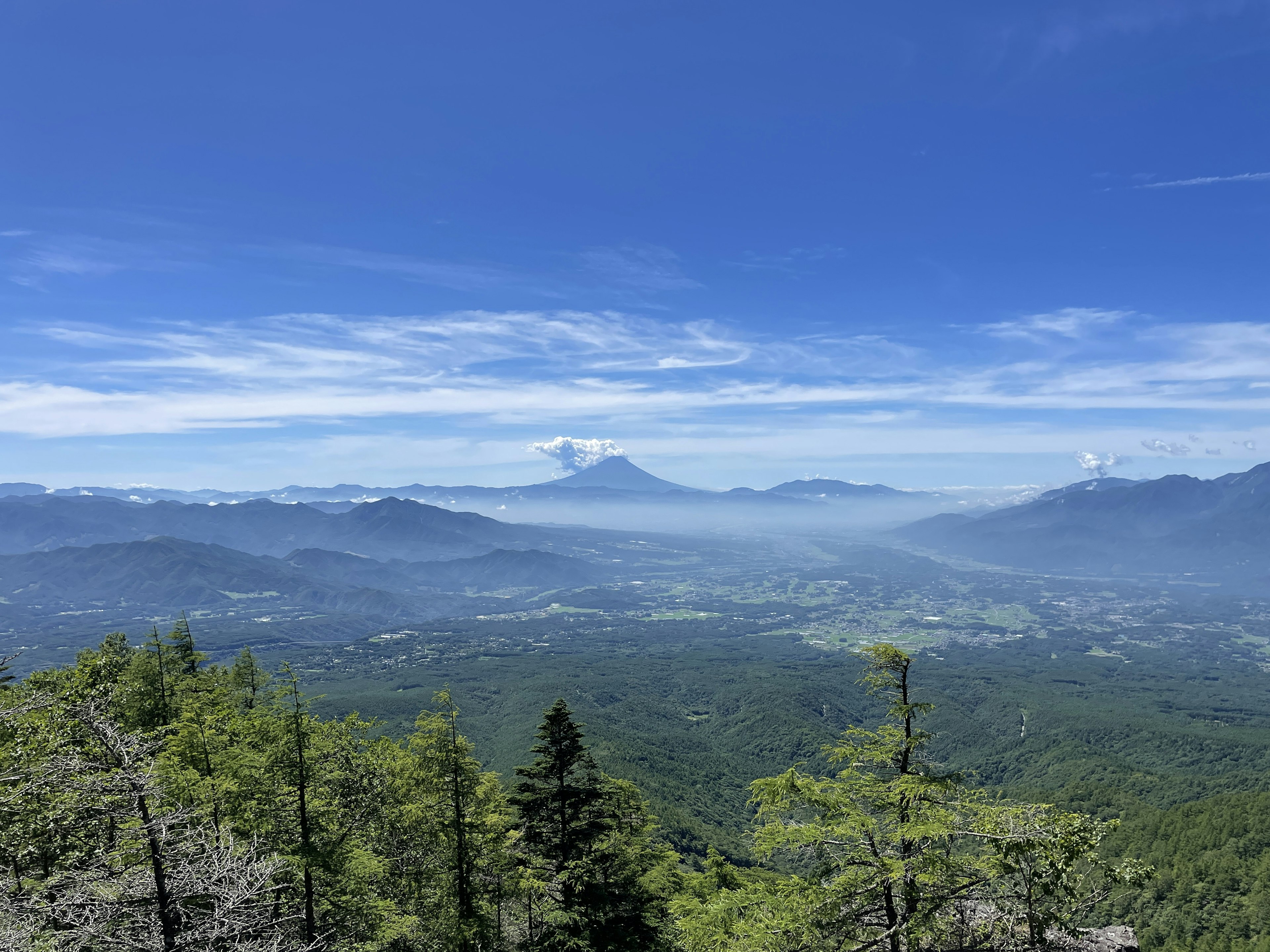 青空の下に広がる緑豊かな山々と遠くに見える火山