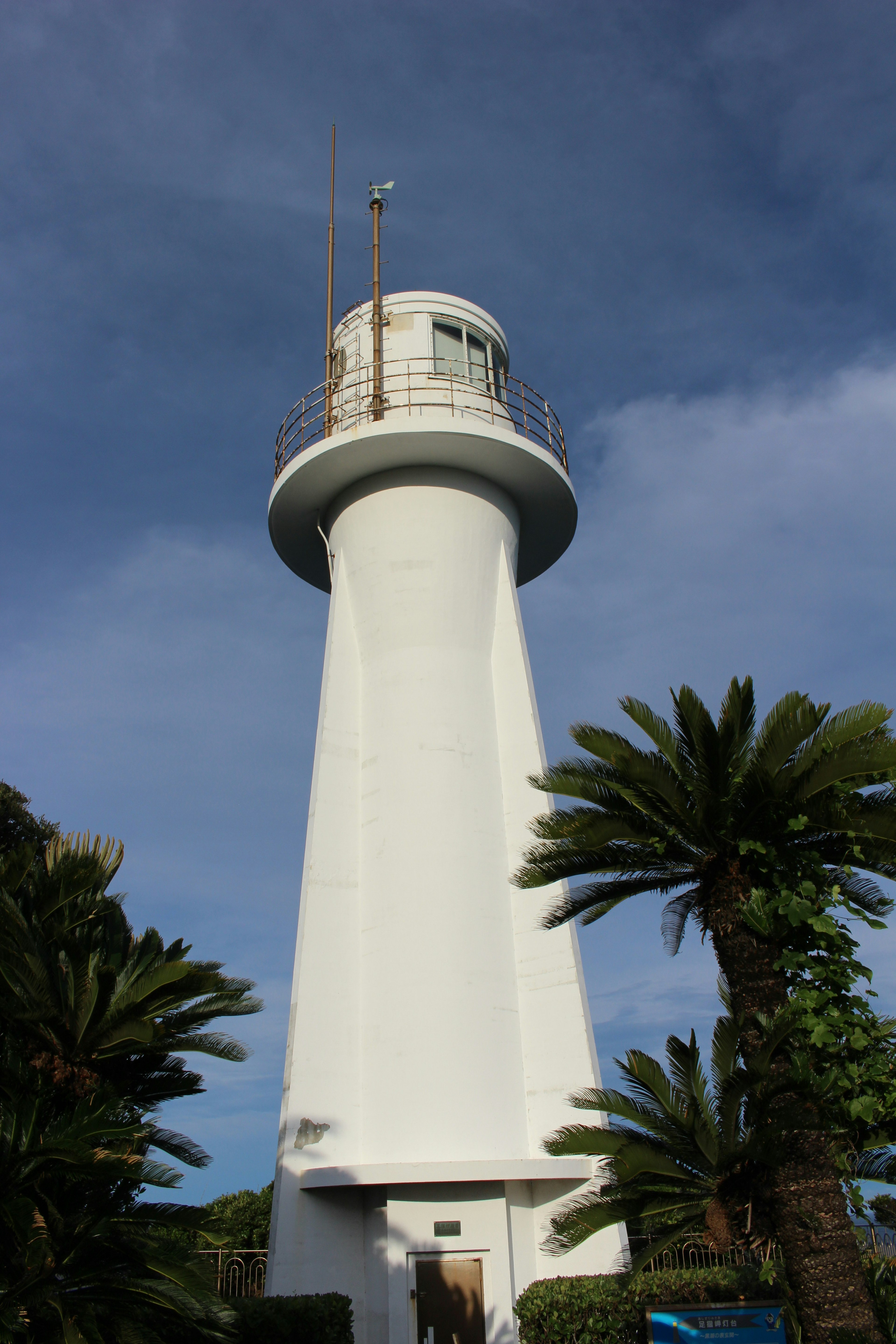 White lighthouse surrounded by palm trees under a blue sky