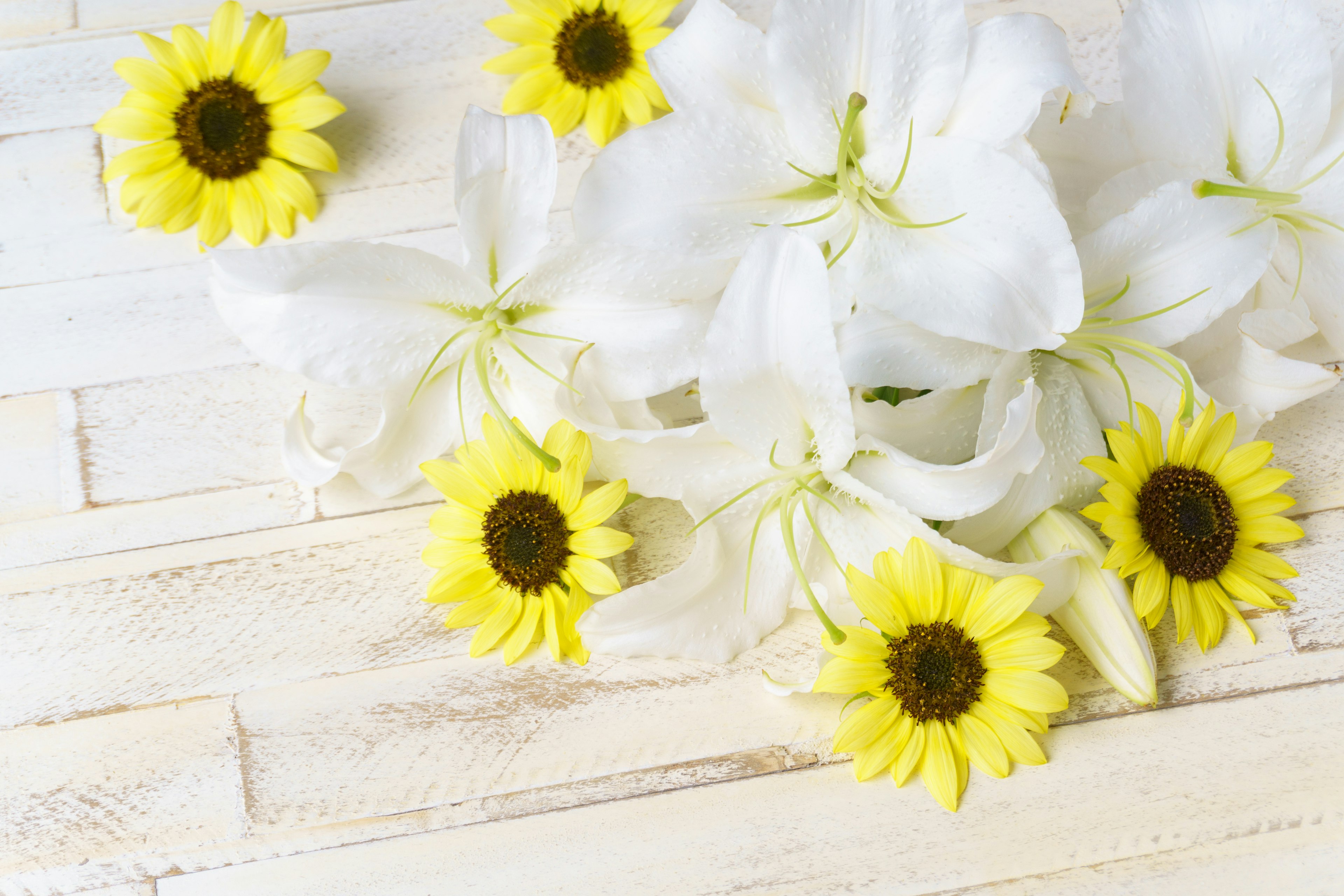 Arrangement of white lilies and yellow sunflowers on a wooden surface