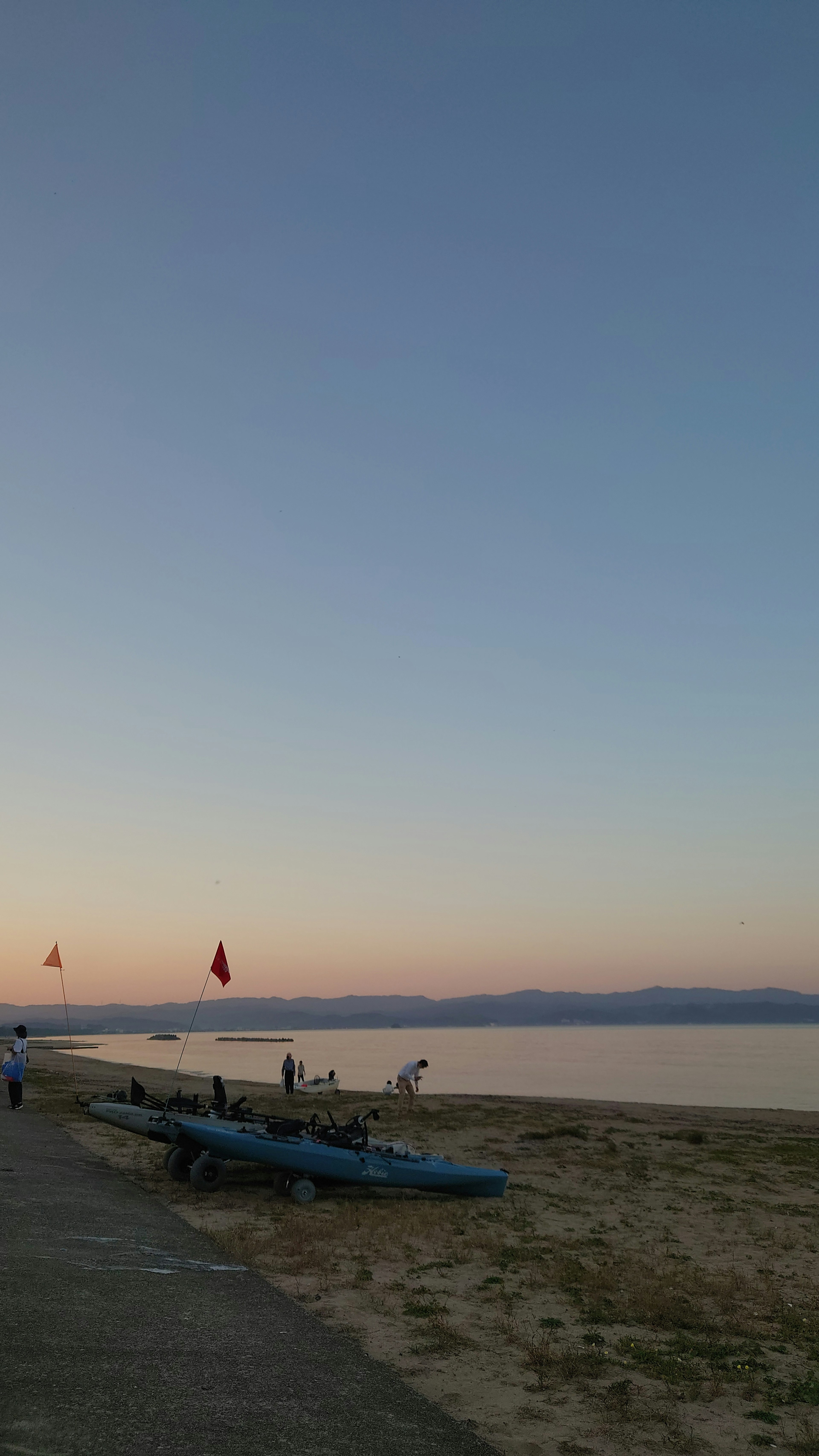 夕暮れ時の湖の岸に並ぶカヤックと人々