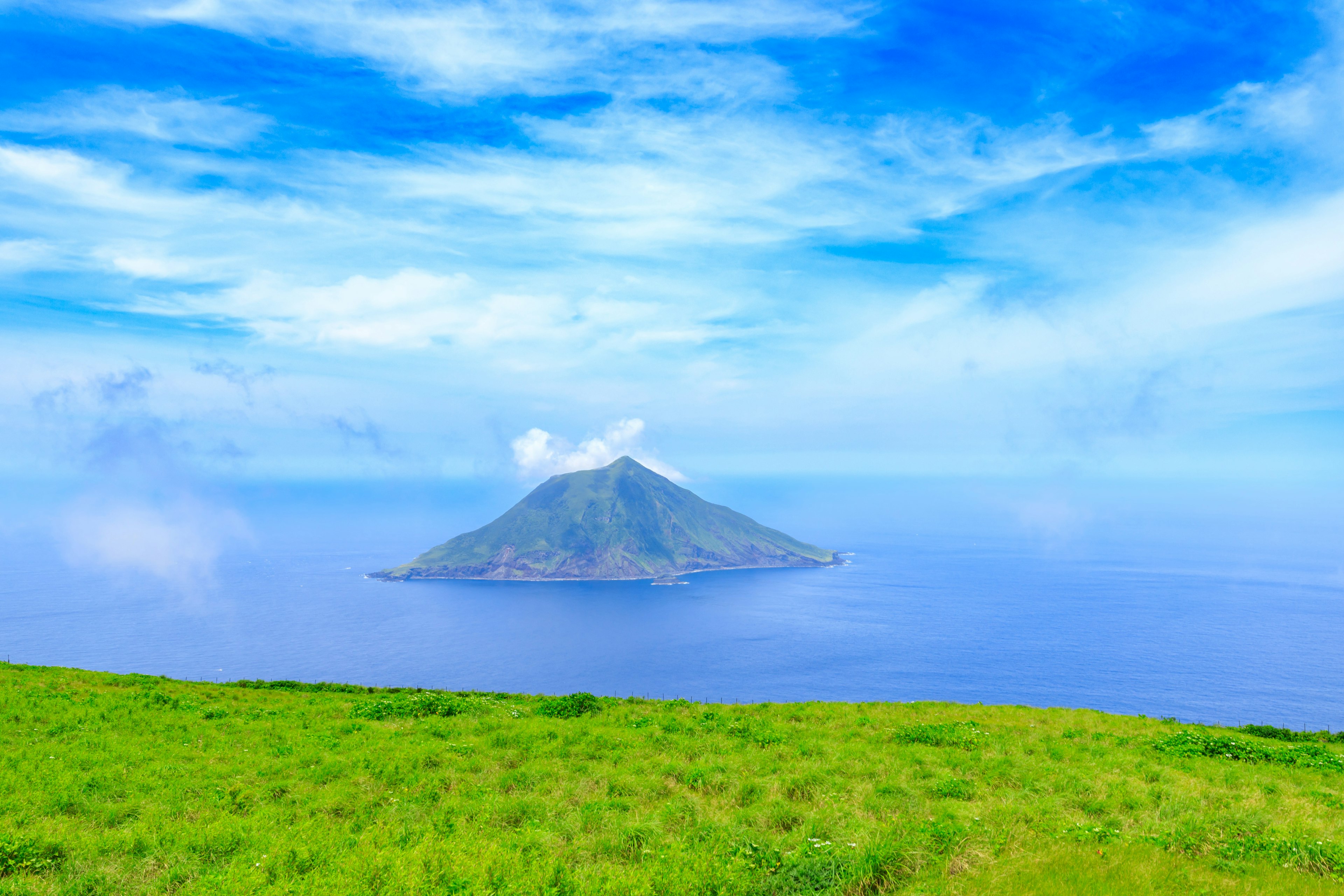 Scenic view of a green meadow with a small island under a blue sky