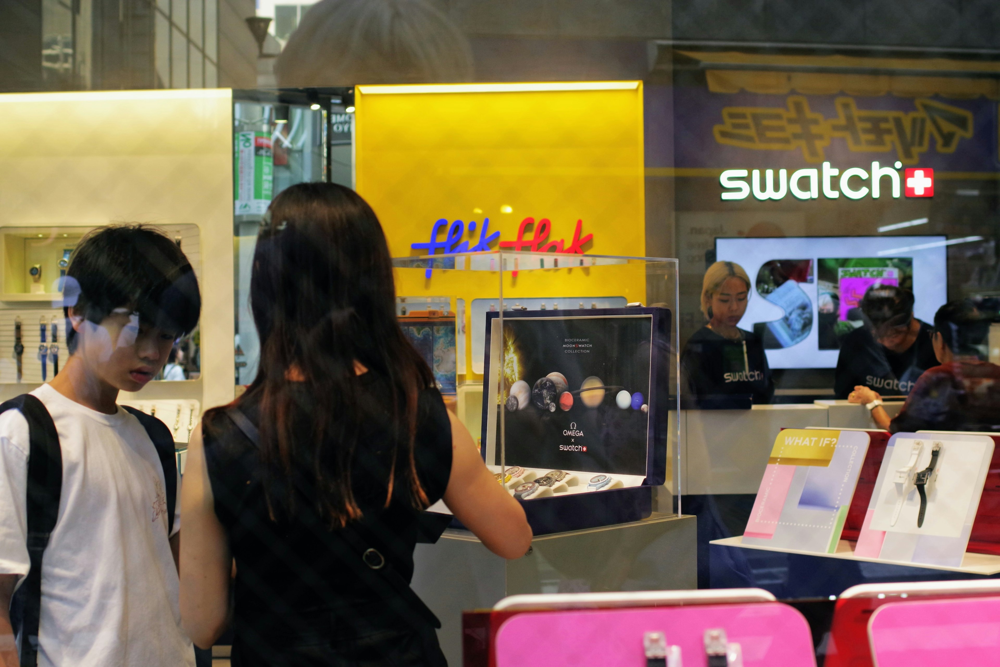 Personas eligiendo relojes en una tienda Swatch con un fondo amarillo brillante