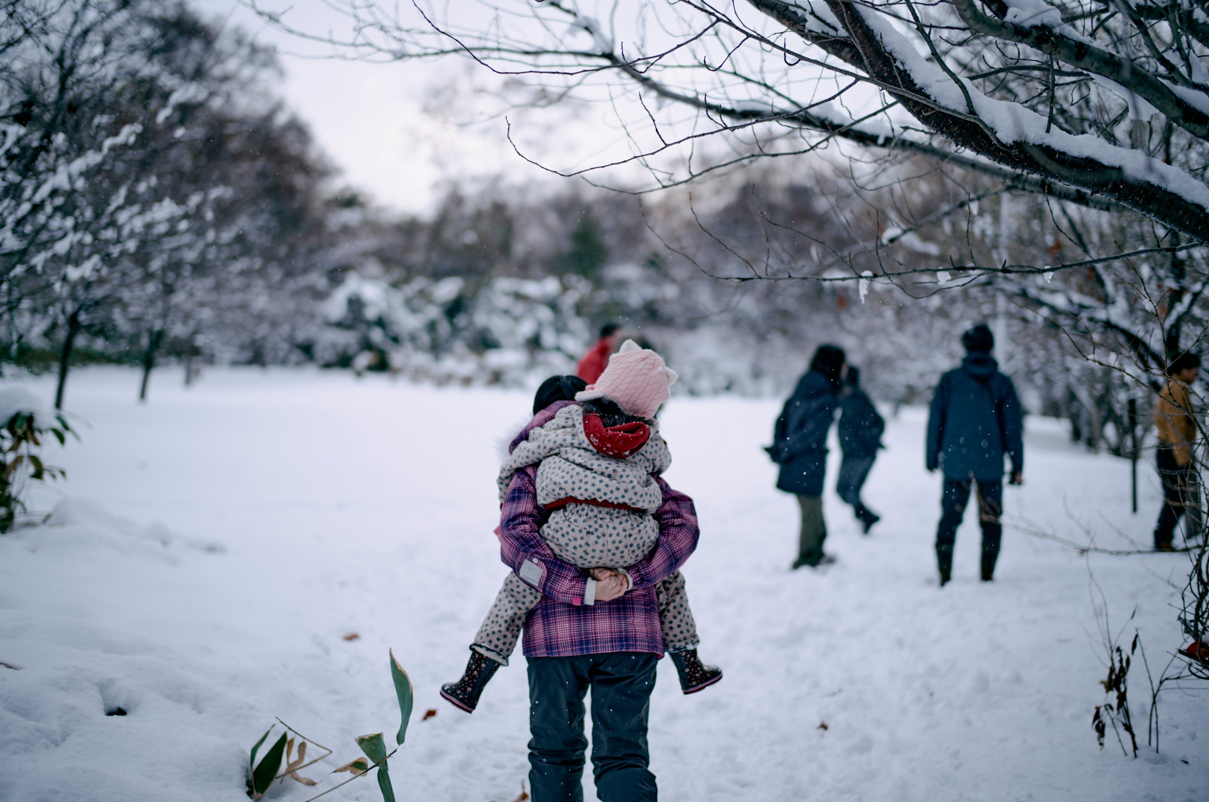 雪の中で子供を背負っている親とその後ろに歩く人々のシーン