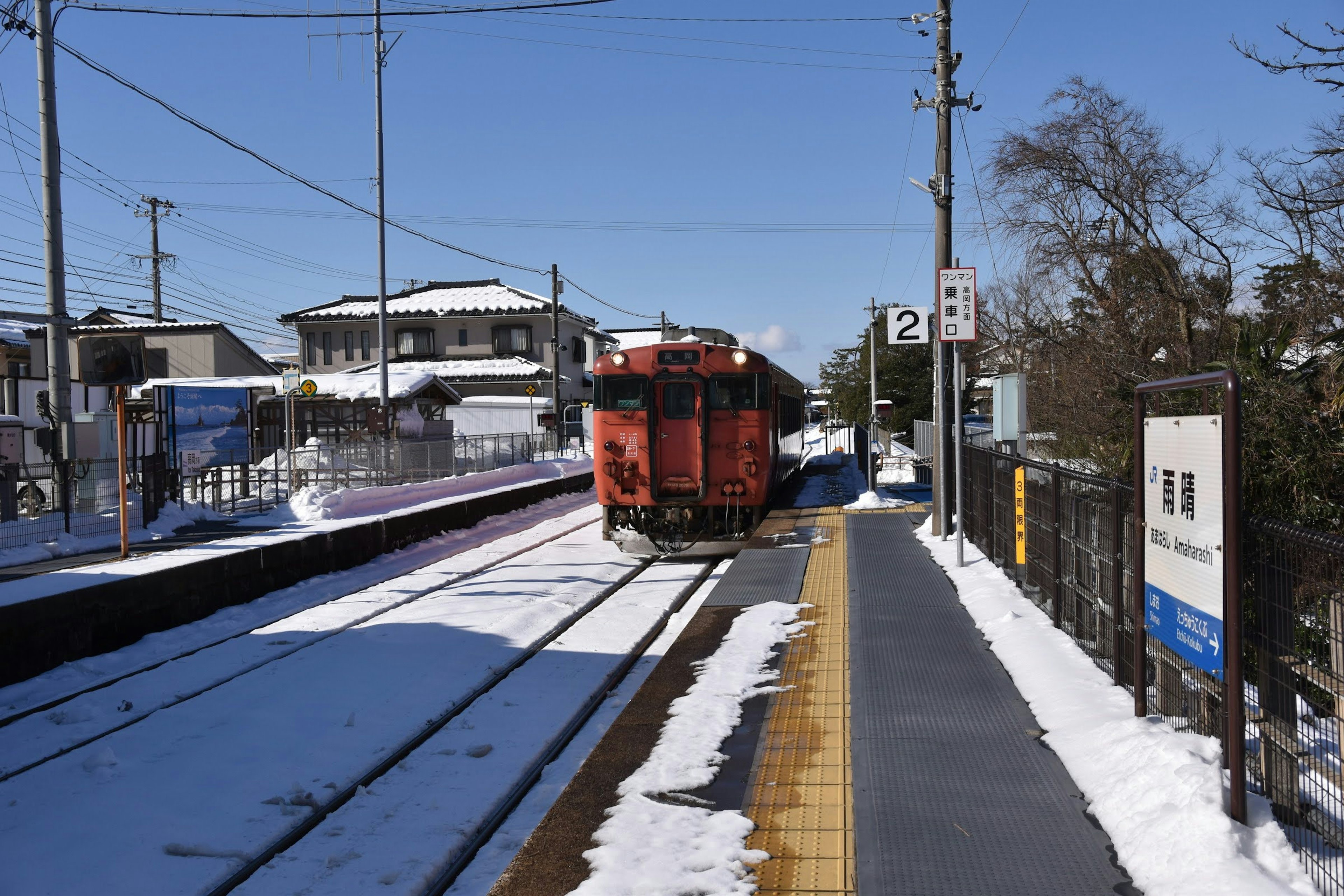 Red train stopped at a snowy station under a clear blue sky