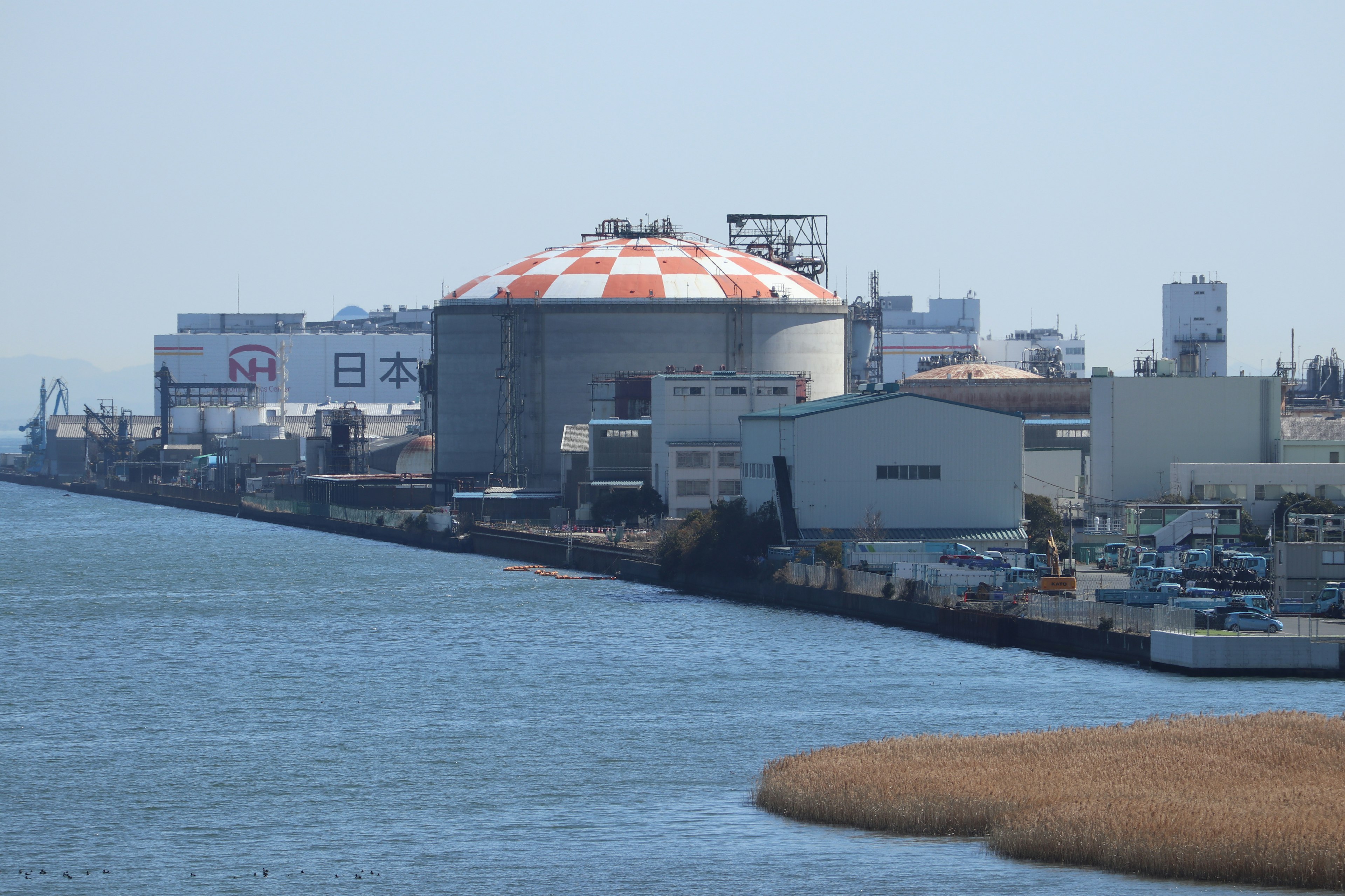 A view of a riverside industrial area featuring a red and white roofed facility and nearby buildings