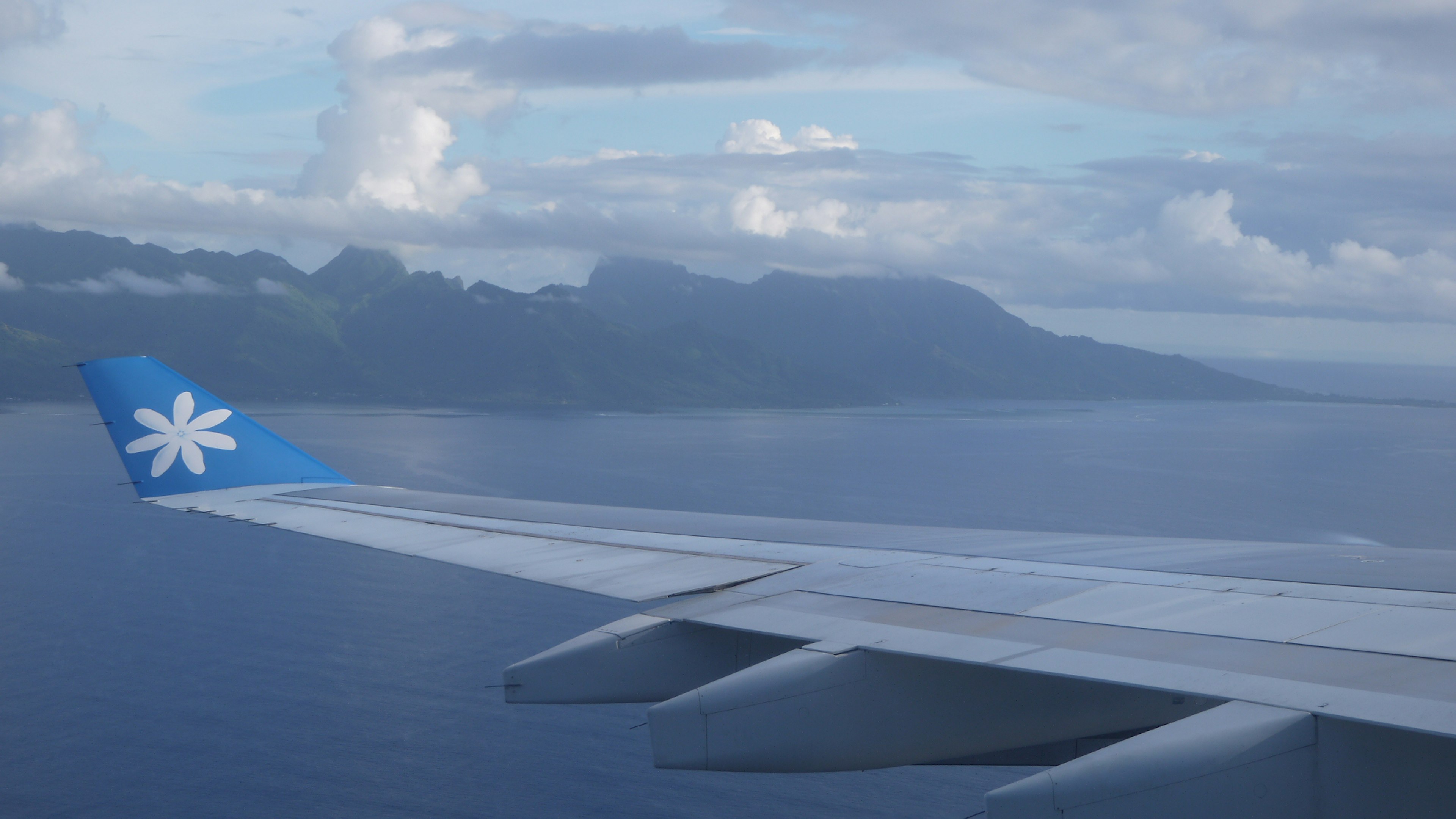 飛行機の翼から見える青い海と山々の景色