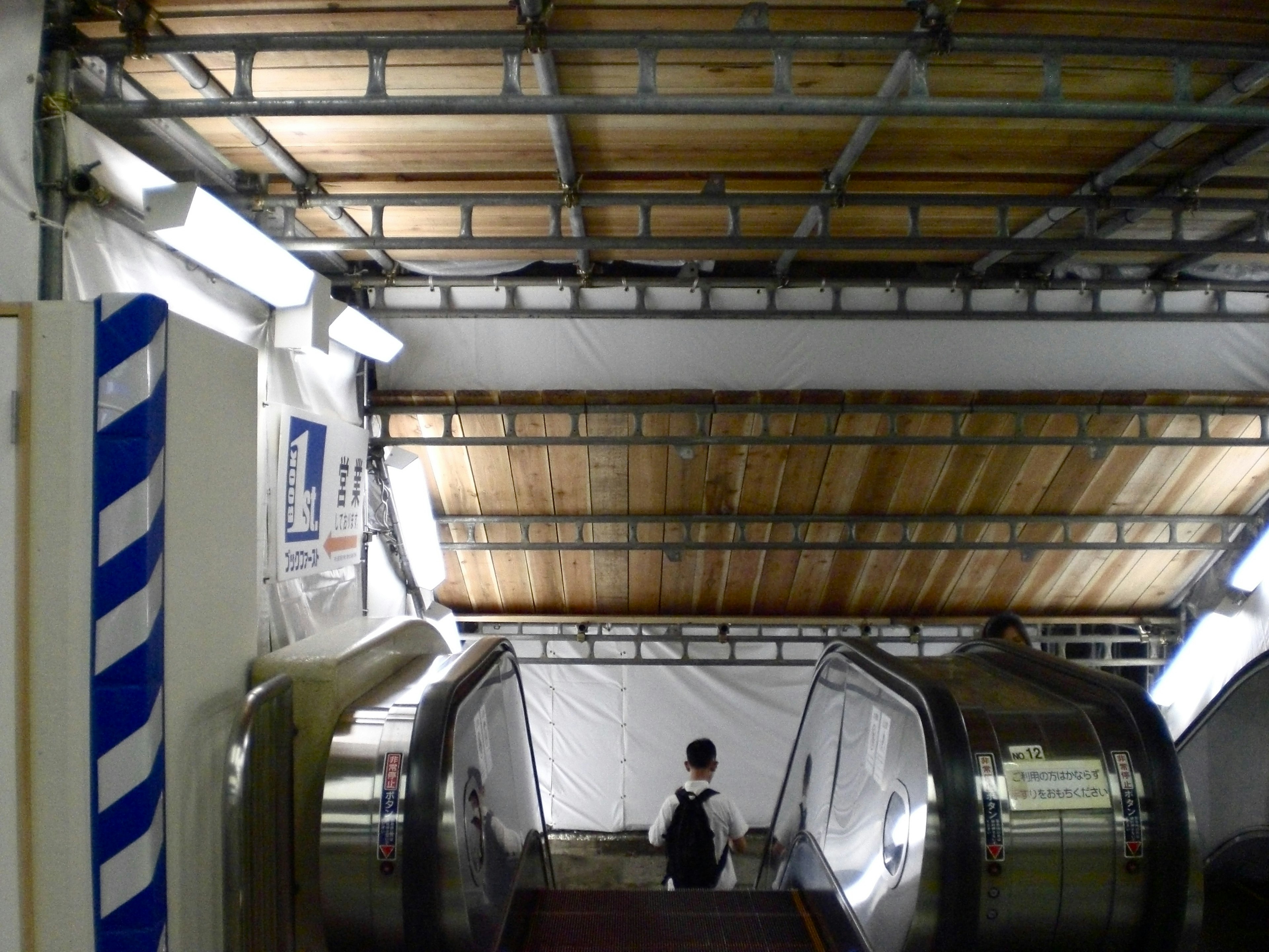 Vista desde la parte inferior de una escalera mecánica con un techo de metal paredes blancas y un techo de madera