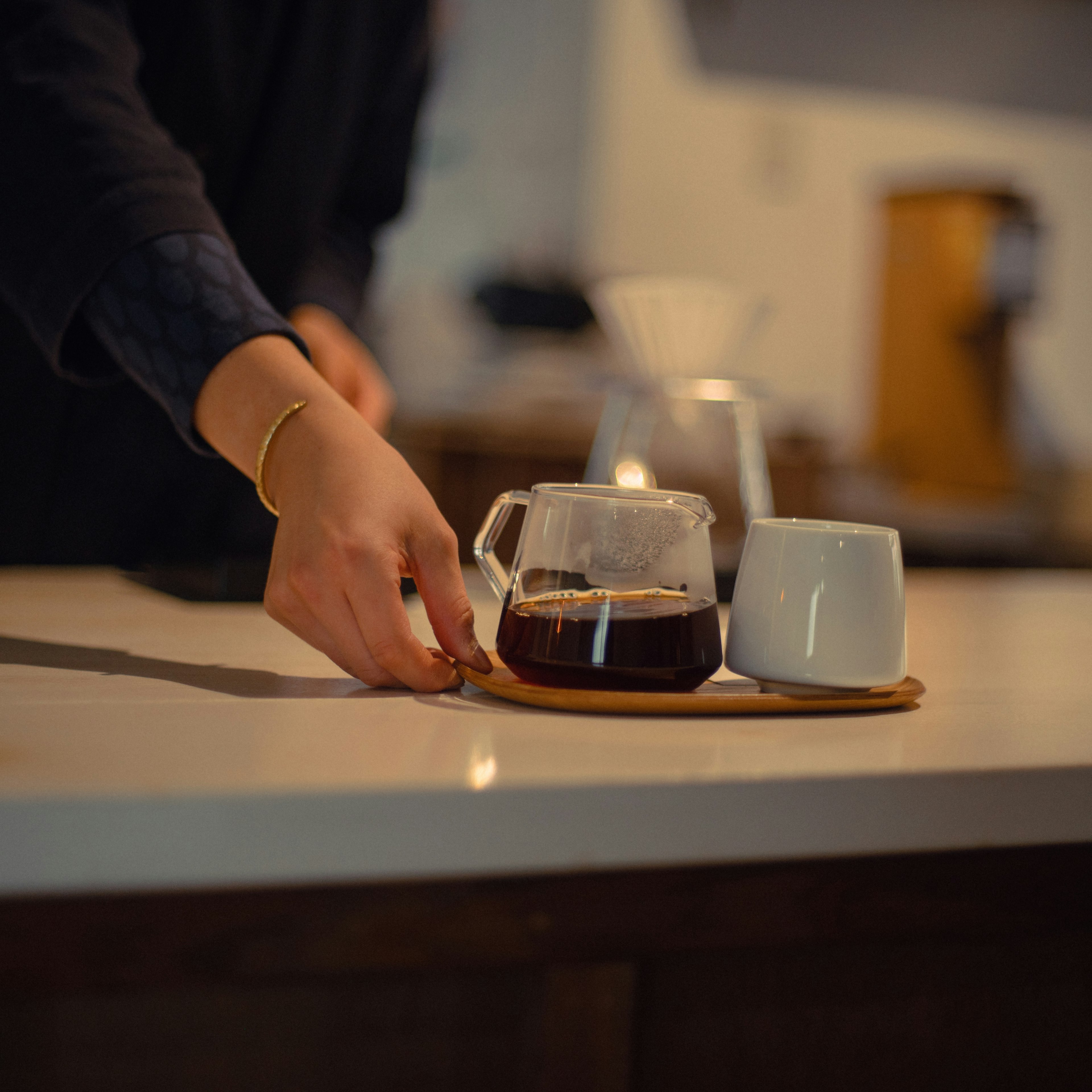 Una mano sirviendo café en una taza blanca sobre una bandeja de madera