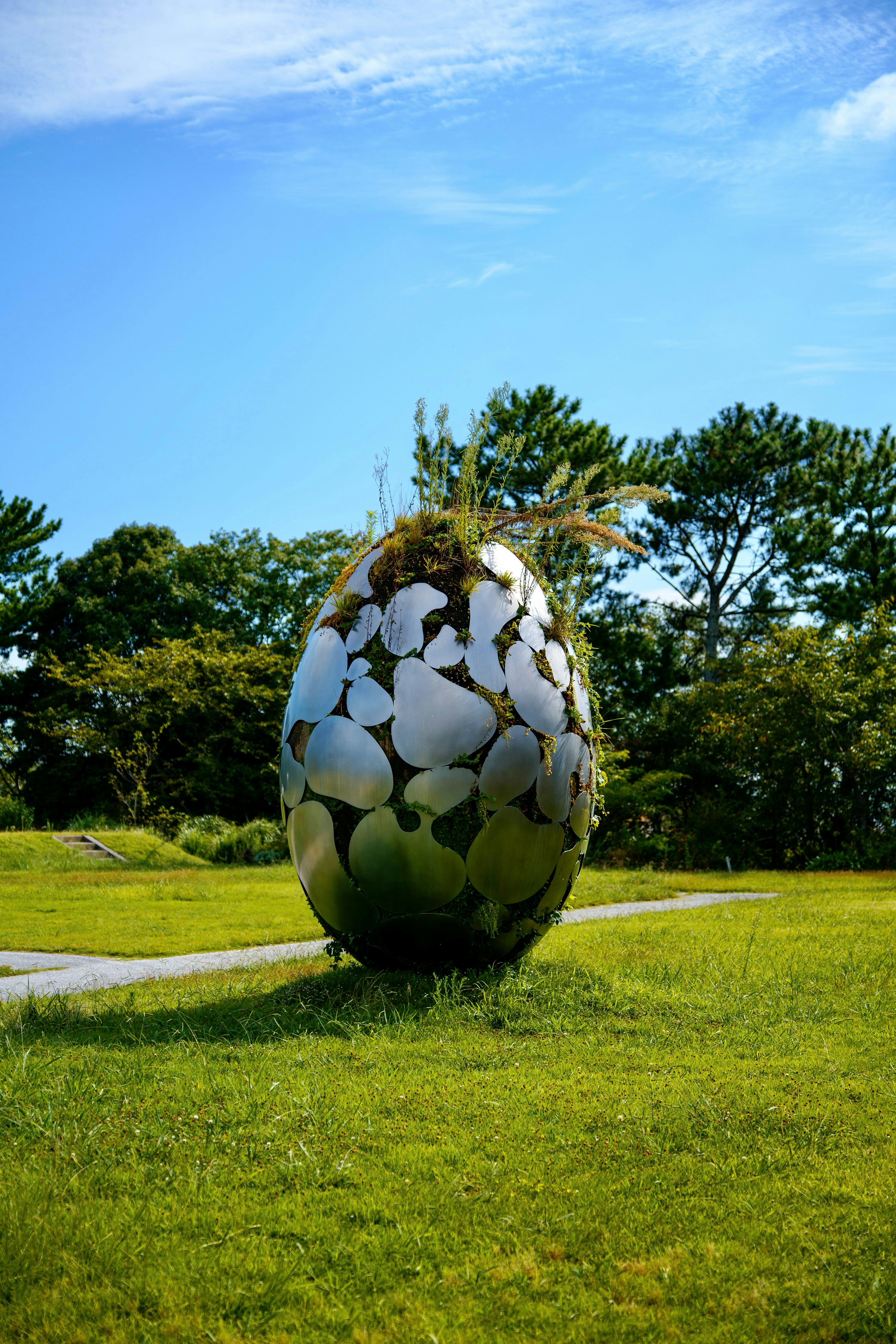 緑の草の上に立つ大きな卵型の彫刻で、卵の上には植物が生えている