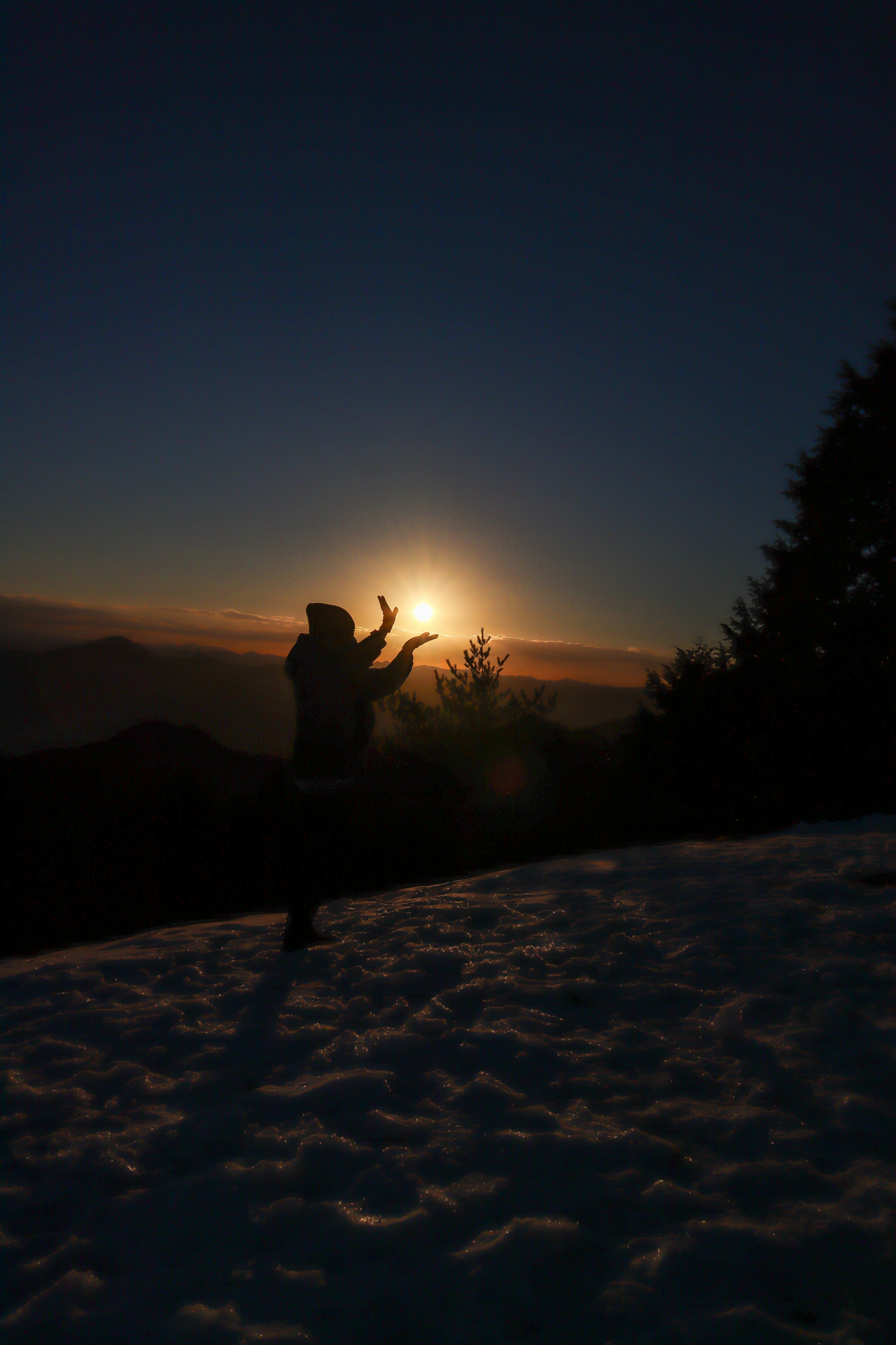 Silhouette einer Person, die auf Schnee posiert, mit Sonnenaufgang im Hintergrund