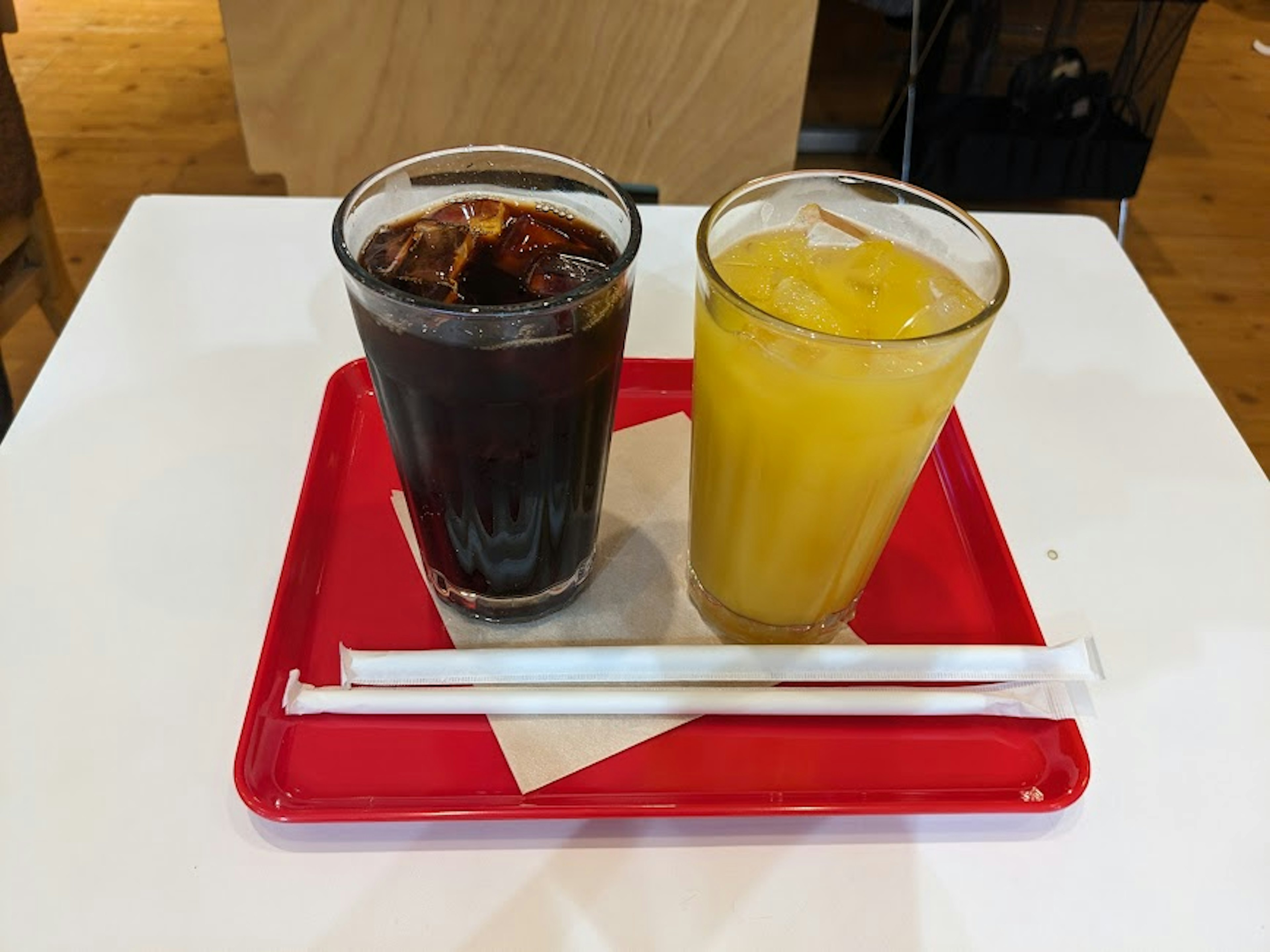 Two drinks of iced coffee and orange juice on a red tray