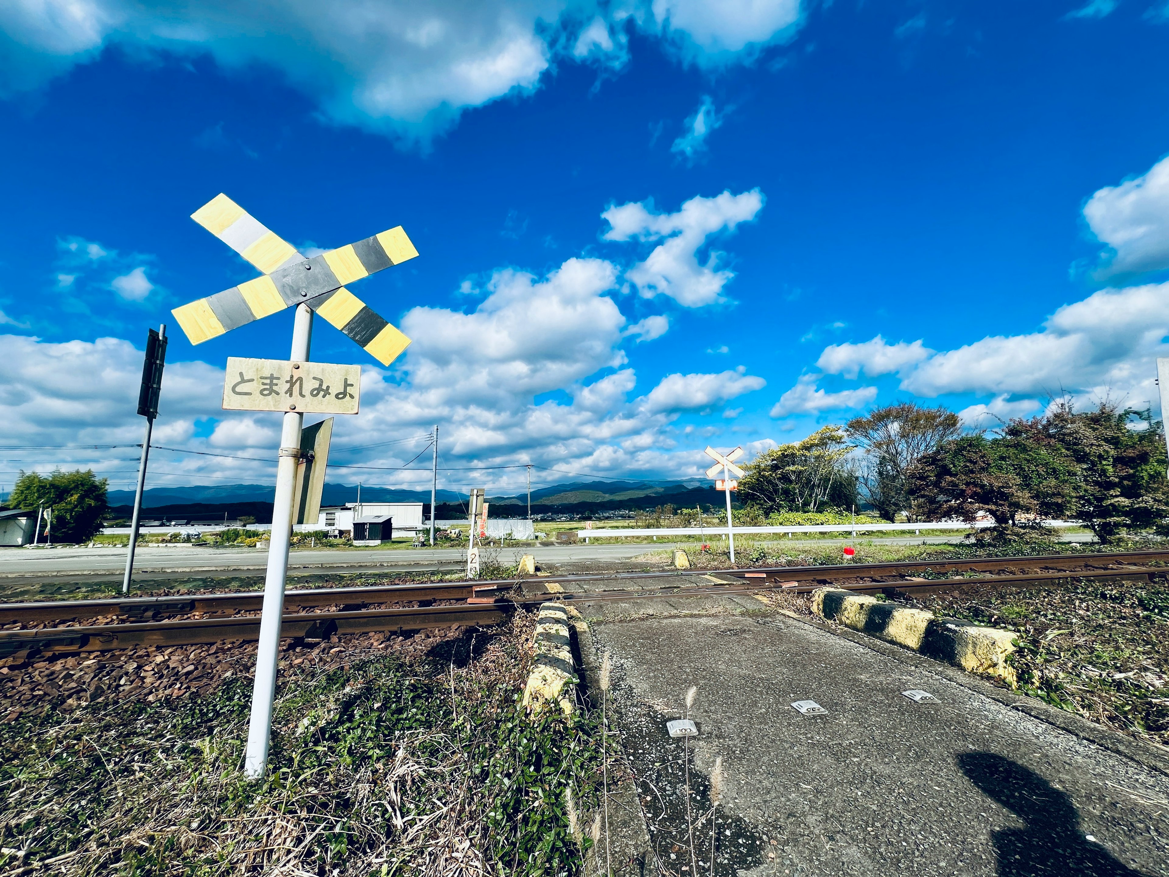 青い空と白い雲の下にある鉄道踏切の風景 目立つ黄色の標識と線路が見える