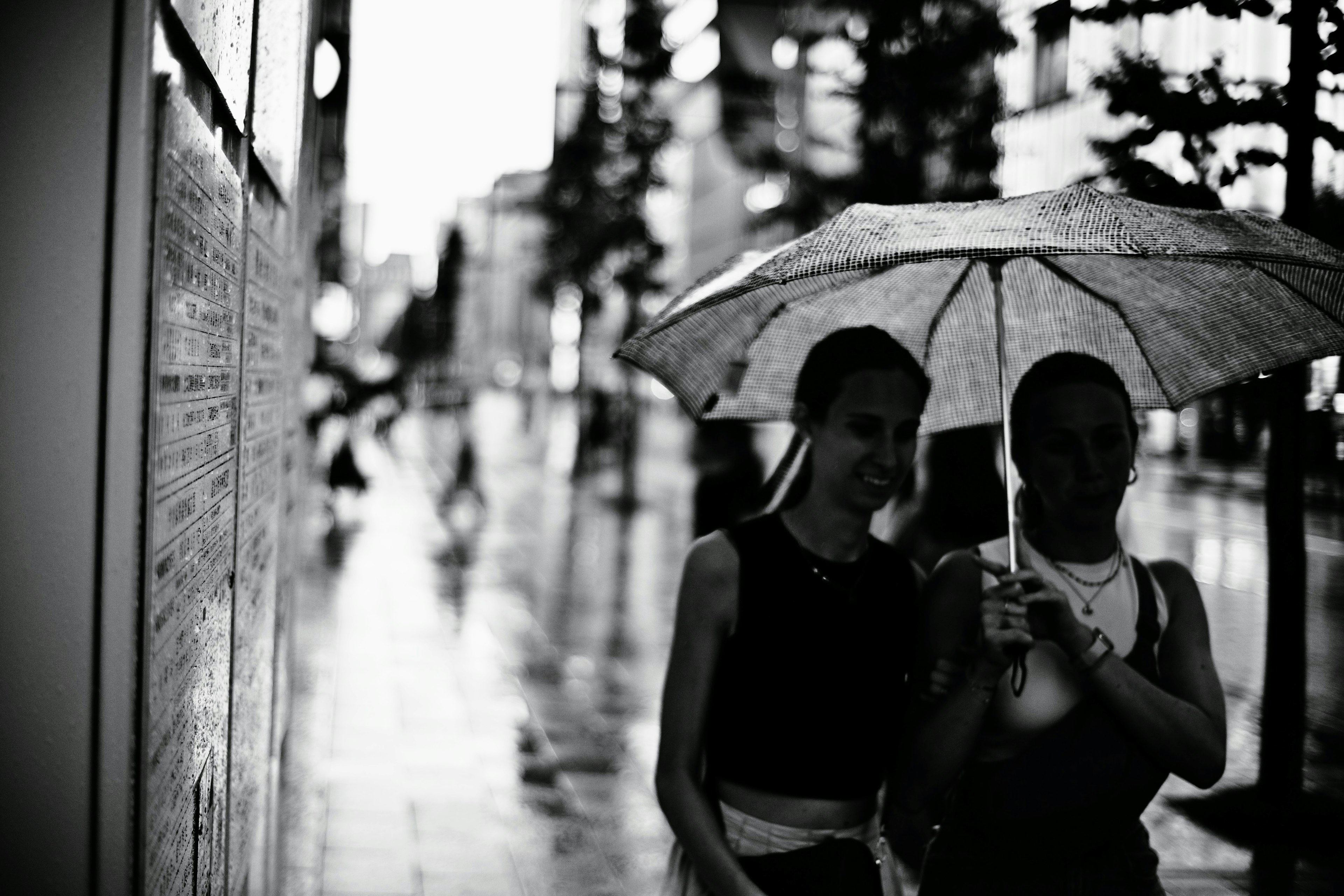 Schwarzweißfoto von zwei Frauen, die im Regen unter einem Regenschirm gehen