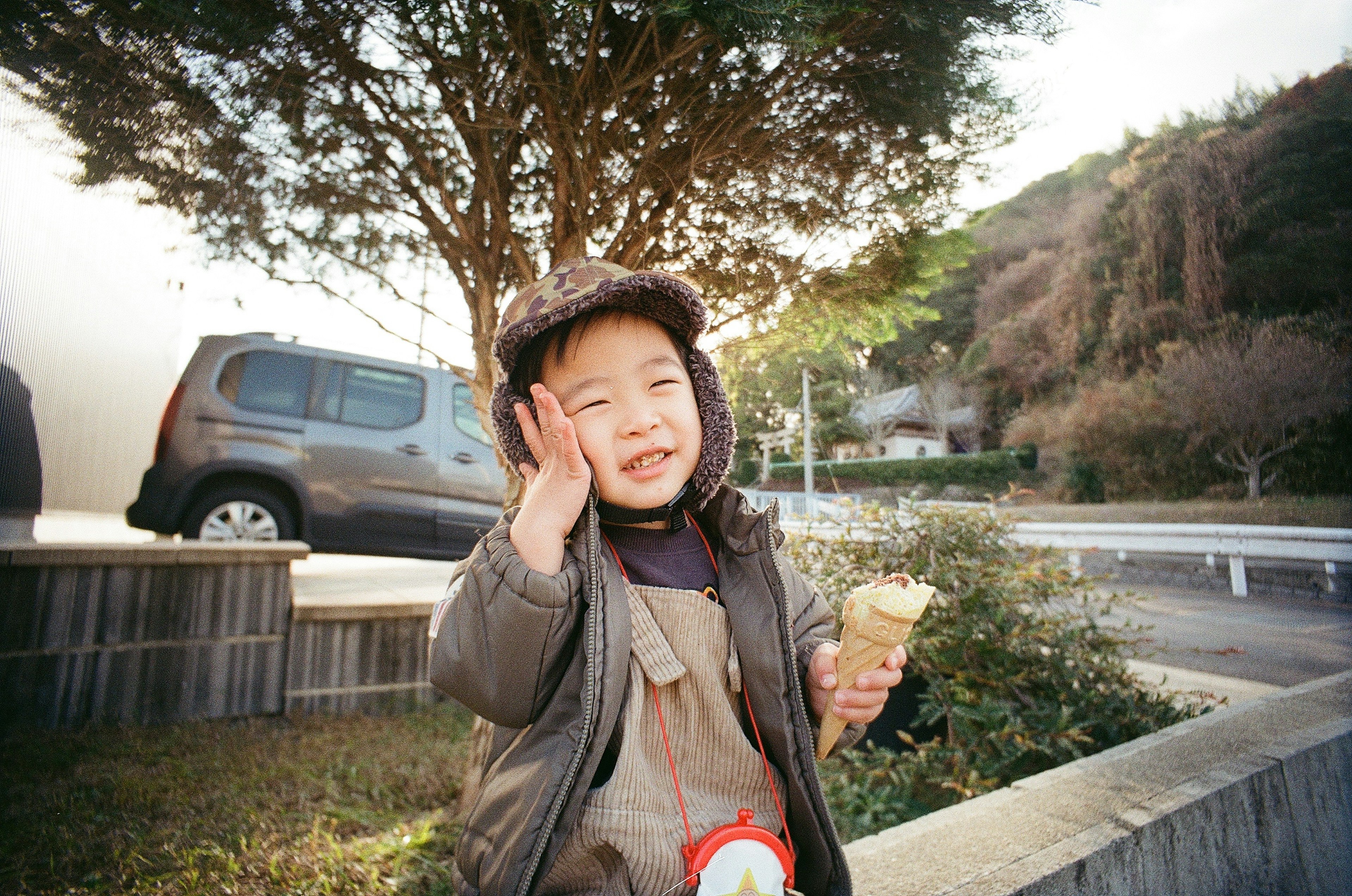 A child waving happily while holding an ice cream in a park