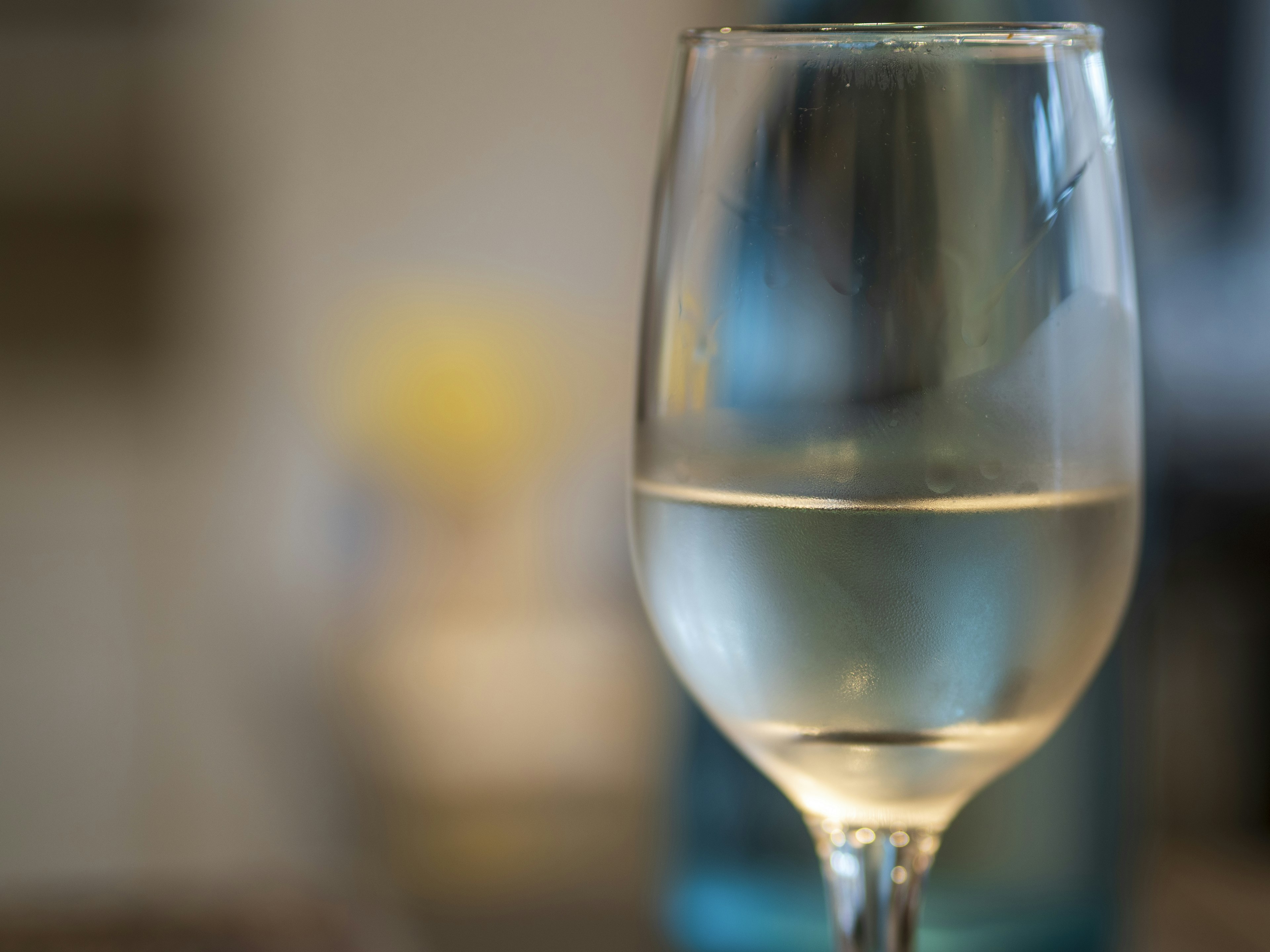 Un vaso de agua clara con una botella azul al fondo